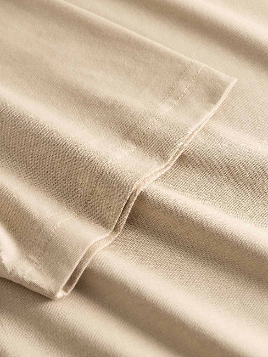 Close-up of the hem and stitching on the Gabba GABdune Logo GOTS SS T-Shirt - Safari. The seam and texture of the soft, GOTS-certified beige cotton highlight its neat double-row stitching.