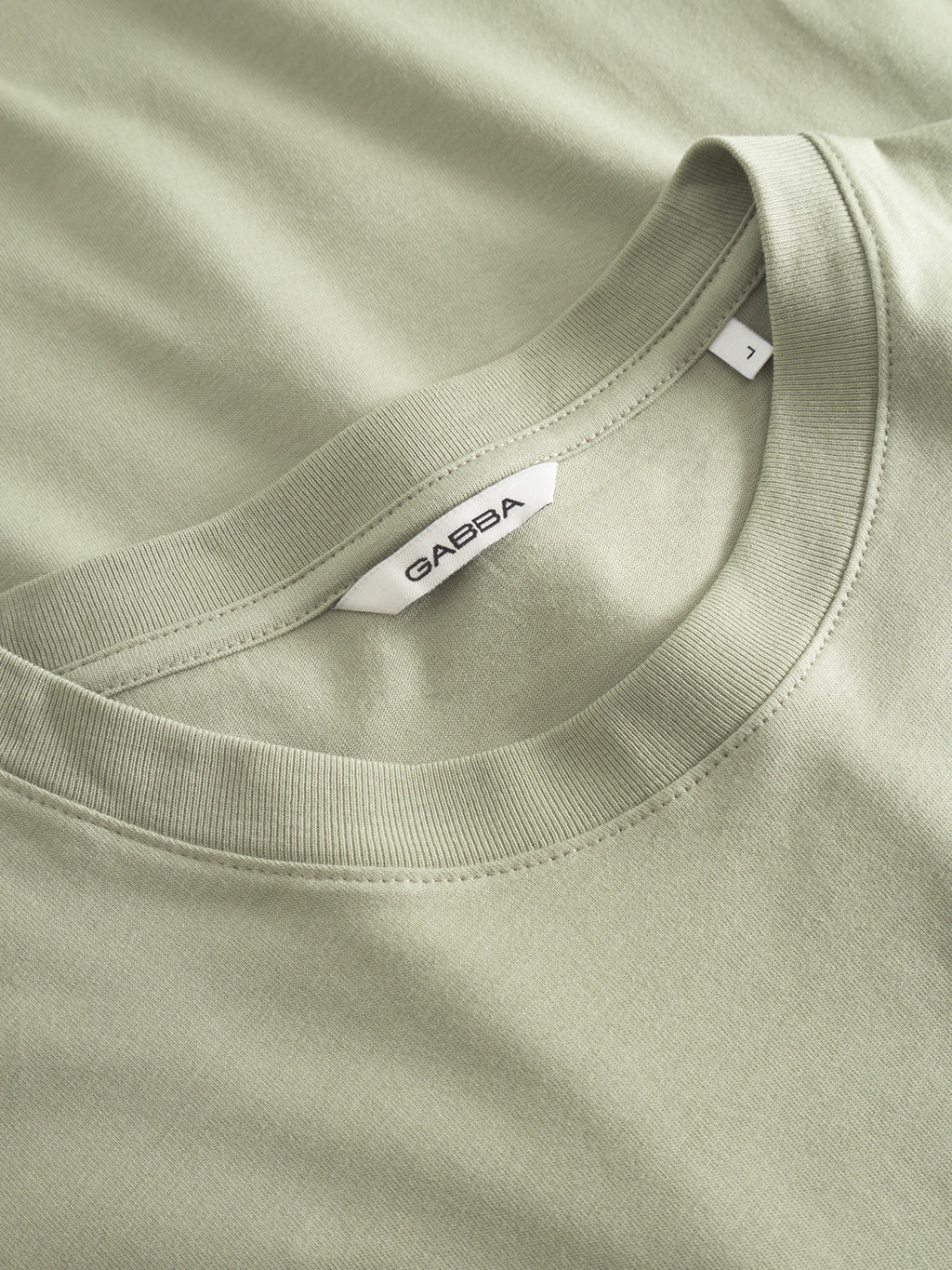 A close-up of the Gabba GABdune Logo GOTS SS T-Shirt in light green, highlighting the collar, stitching details, and an inner white label with the Gabba brand name.