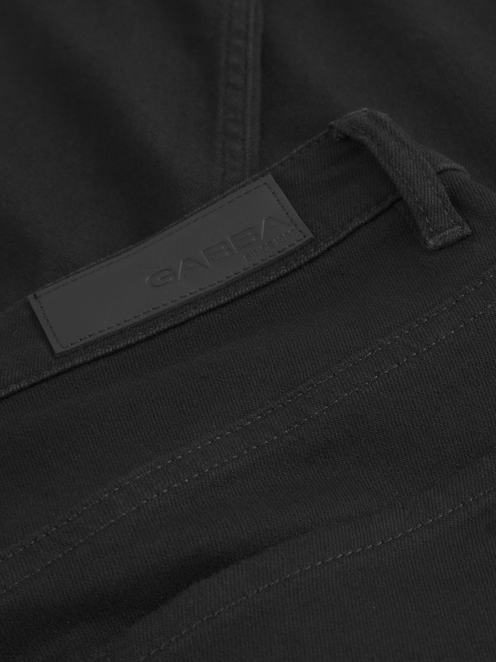 Close-up of GABmarc Sword - Black Denim jeans by Gabba, featuring intense black fabric, detailed stitching, a belt loop, and a black leather patch embossed with the brand name for a sharp, clean look.
