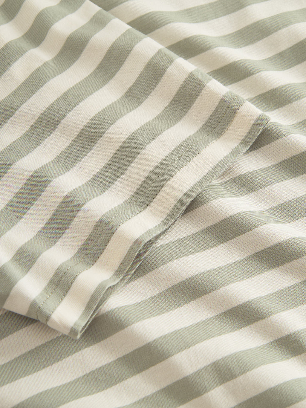 Close-up of the Gabba GABdune Logo Stripes SS GOTS t-shirt, made from GOTS-certified organic cotton, featuring soft green and white horizontal stripes and a folded edge with visible stitching.