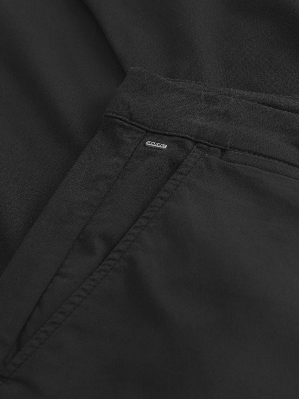 Close-up of the Gabba Paul K3280 Cargo Dale - Black pants shows the front pocket with a metal “Daily” tag and branded buttons. The slim fit design features smooth, matte fabric for a stylish look.