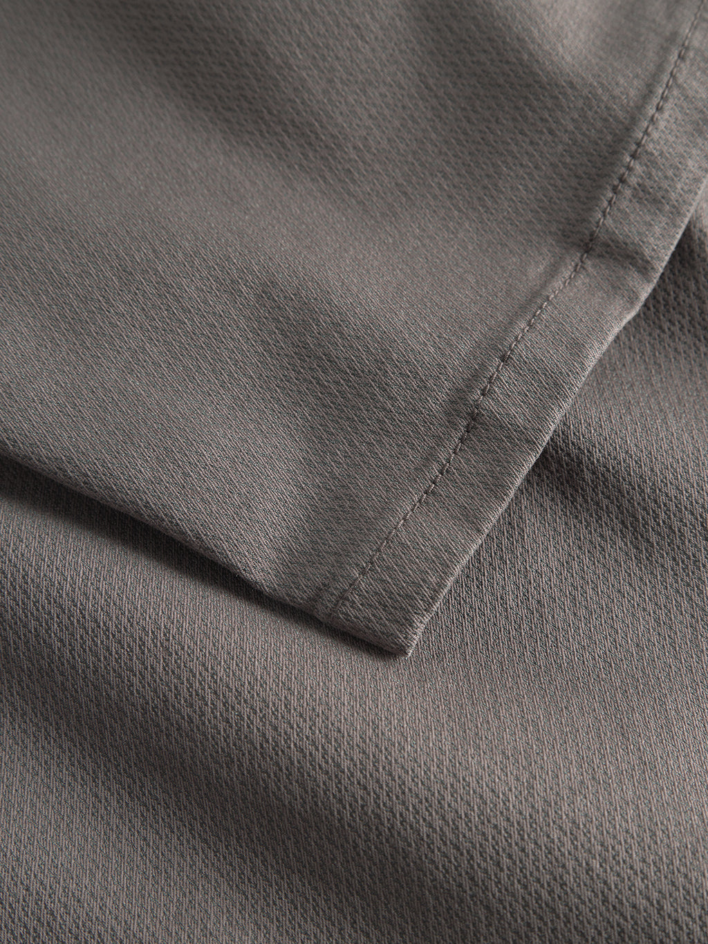 Close-up of the GABpaul K3280 Dale Chino by Gabba in charcoal, highlighting two layers of textured fabric with fine stitching and a subtle grid pattern—features typical of slim chinos with French pockets and tailored leg openings.