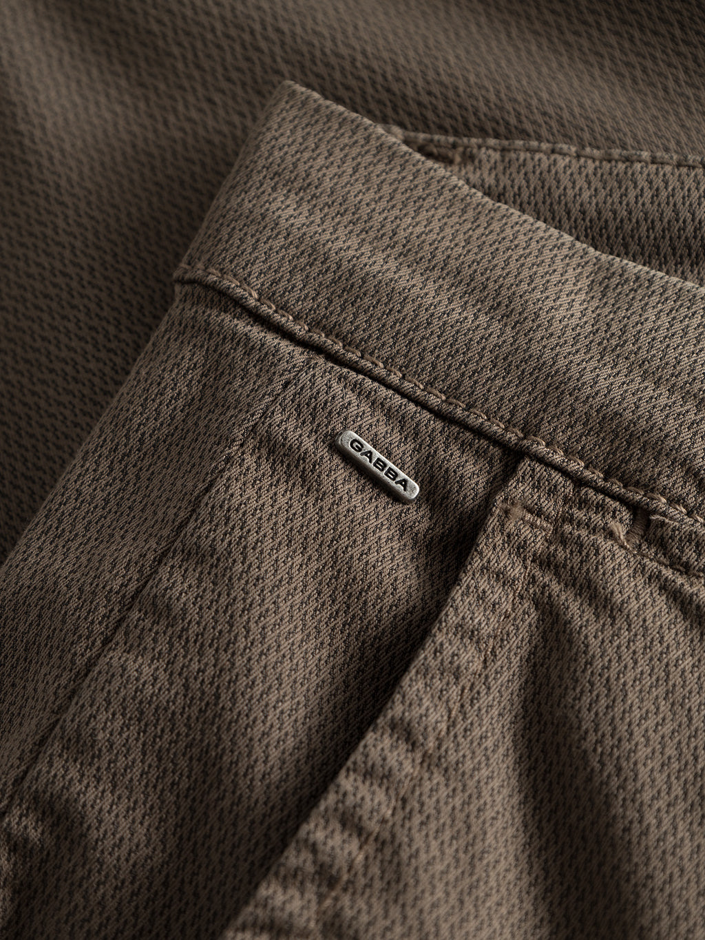 Close-up of Gabba GABpaul K3280 Dale Chino in Crocodile: brown textured slim-fit pants with French pockets, a small metal Gabba tag near the seam, and a subtle repeating diamond-patterned fabric.
