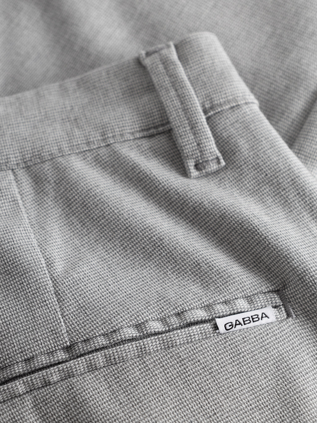 Close-up of Pisa Domo Pants - Monument by Gabba in light grey textured fabric, featuring a belt loop, waistband, and back pocket with a small white Gabba tag—crafted for lasting quality.