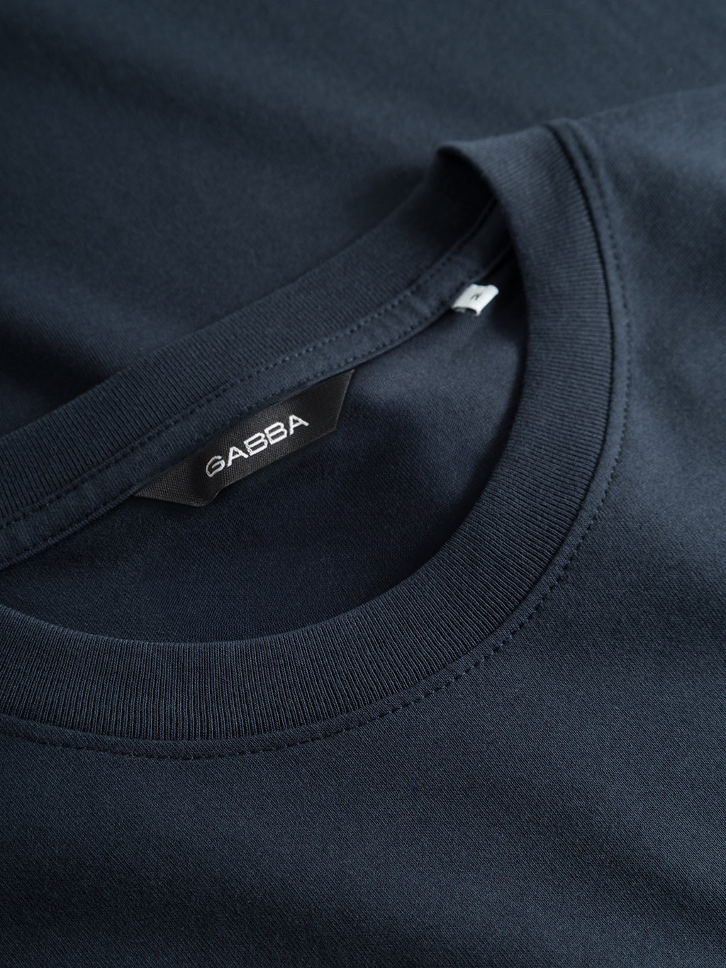 Close-up of the Gabba GABdune Logo GOTS SS T-Shirt in Total Eclipse, featuring a navy blue crew neck, visible stitching details, and a black Gabba label sewn inside the neckline.