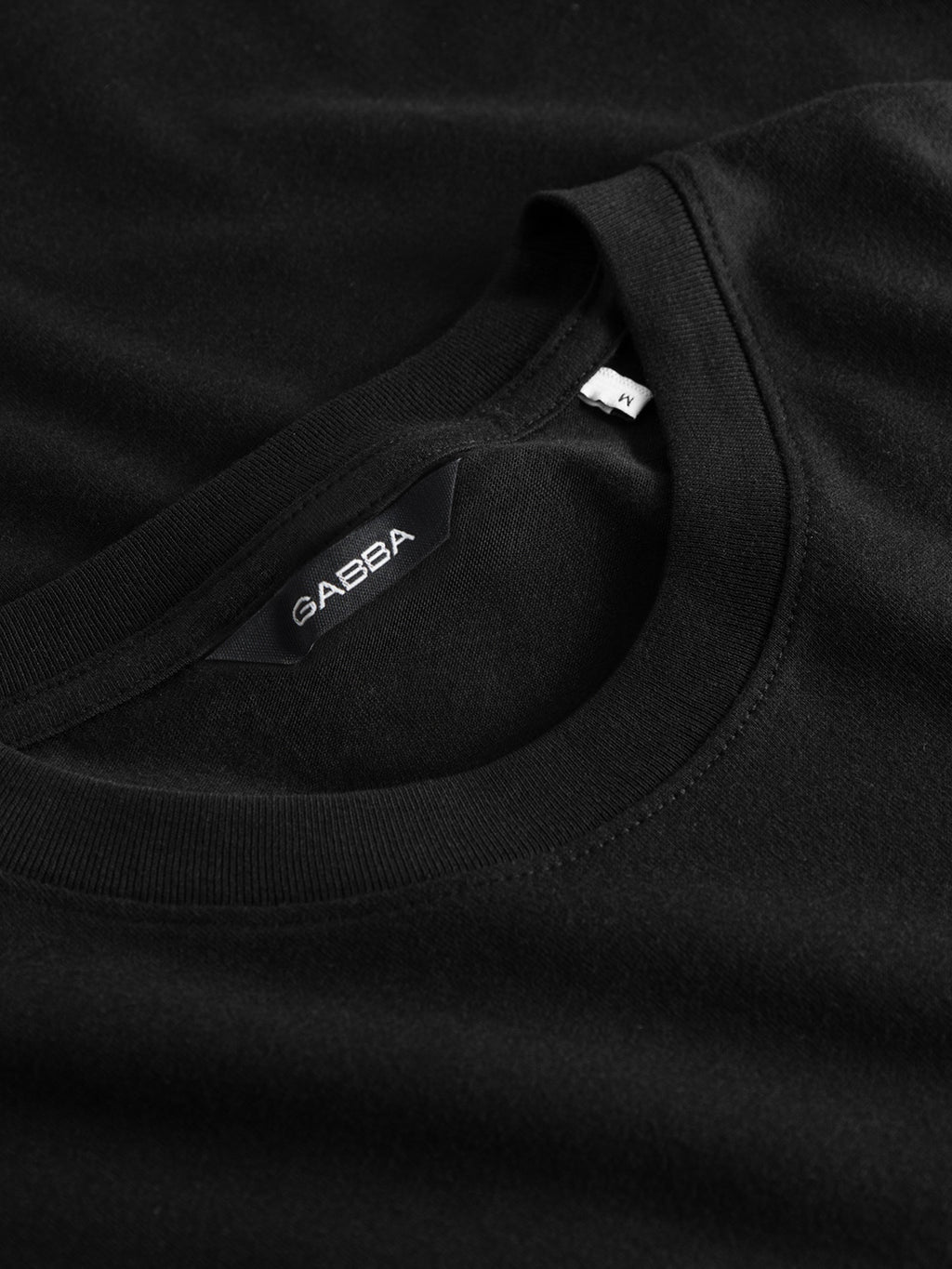 Close-up of a black Gabba GABdune Logo GOTS SS T-Shirt with visible label and XL size tag at the collar, showcasing the organic cotton fabric’s texture and stitching on this classic fit tee.
