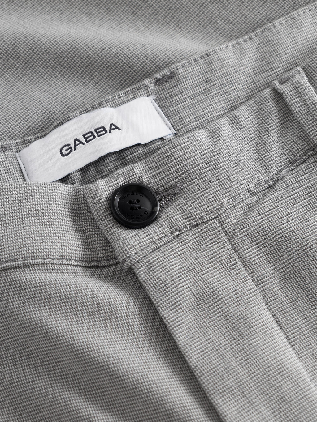 Close-up of Gabba's Pisa Domo Pants in Monument shows their grey fabric, black button, and an inner white label reading 