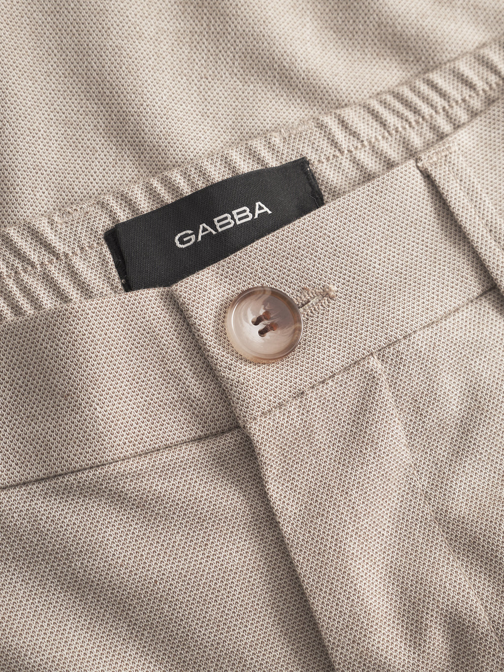 Close-up of Napoli 19 Carre - Sand pants by Gabba, highlighting their beige textured fabric, single brown button, and black Gabba label sewn inside the waistband for a comfortable fit and classic style.