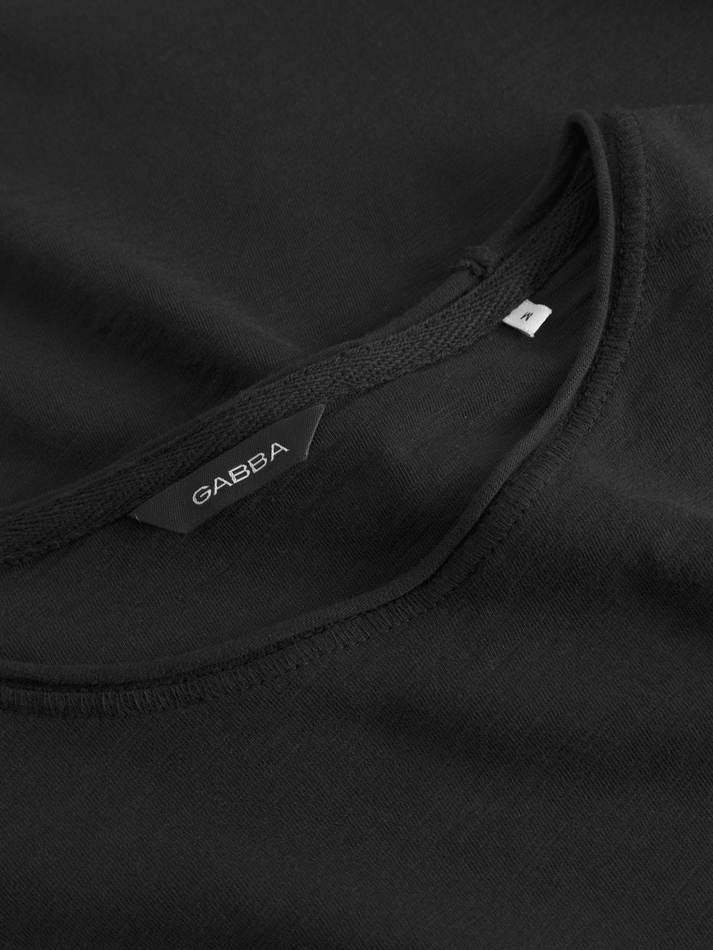 Close-up of the GABkostant New SS - Meteorite t-shirt in black slub fabric, showing its neckline, a woven Gabba brand tag, and an M size label by the collar seam.