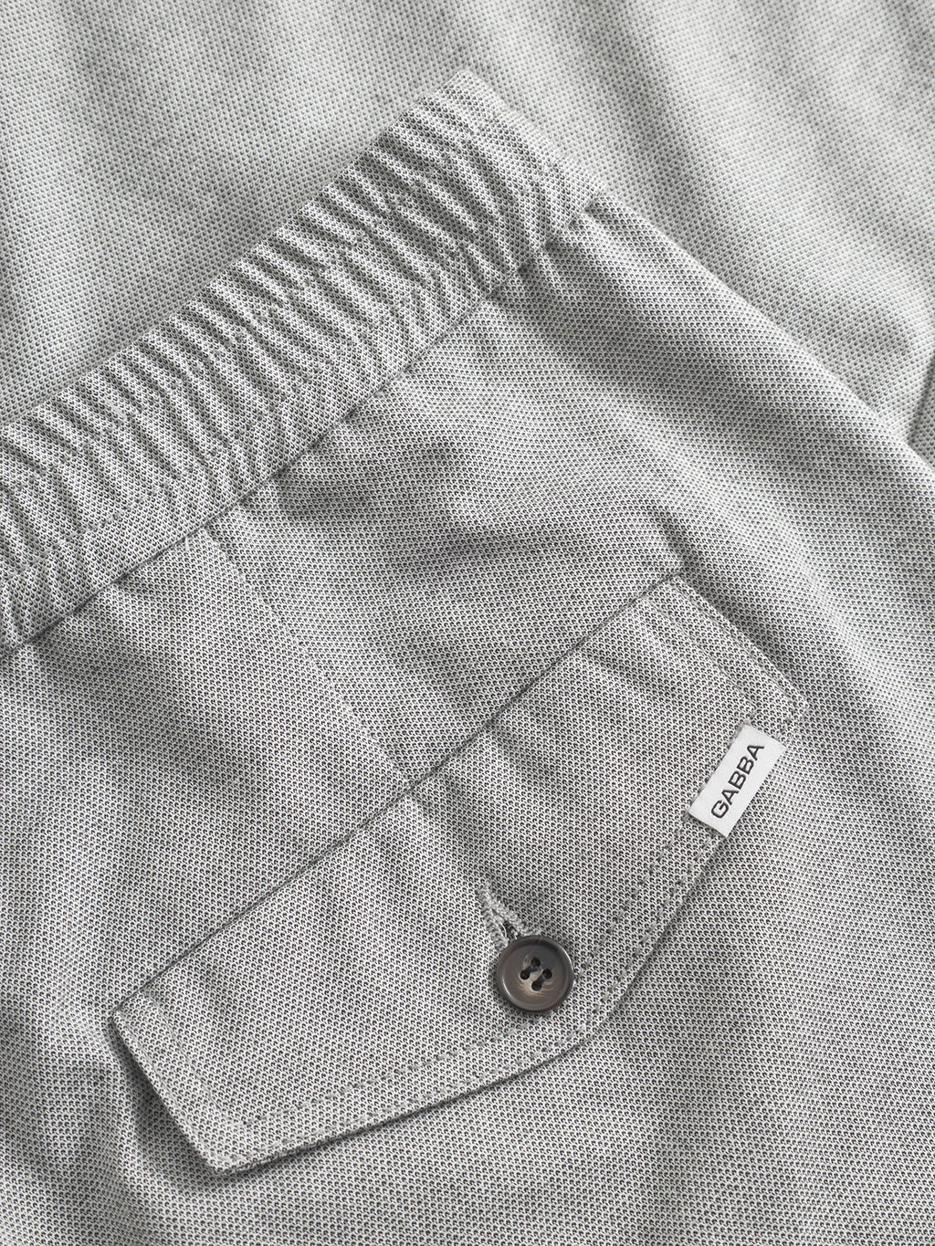 Close-up of Gabba Monza Button Carre - Lt. Grey: light gray textured fabric, relaxed straight pants with elastic waist, back pocket with button, and a sewn-on white 
