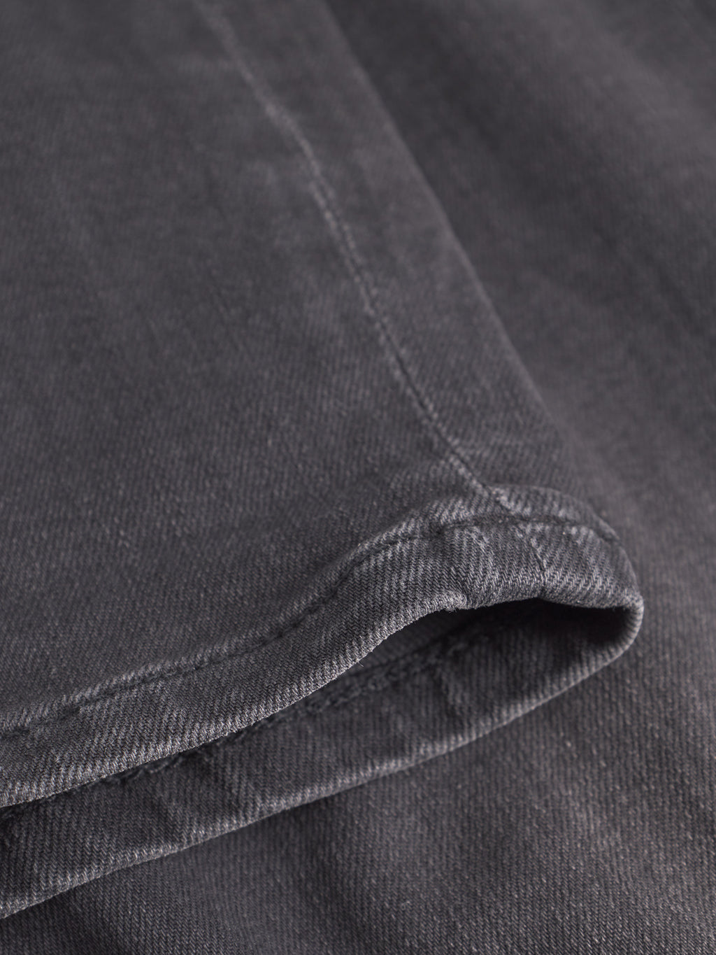 Close-up of a folded edge of dark grey, textured fabric—detailed stitching and a soft, worn look evoke the laid-back style of your favorite GABBA GABrey Thor Jeans in denim wash.