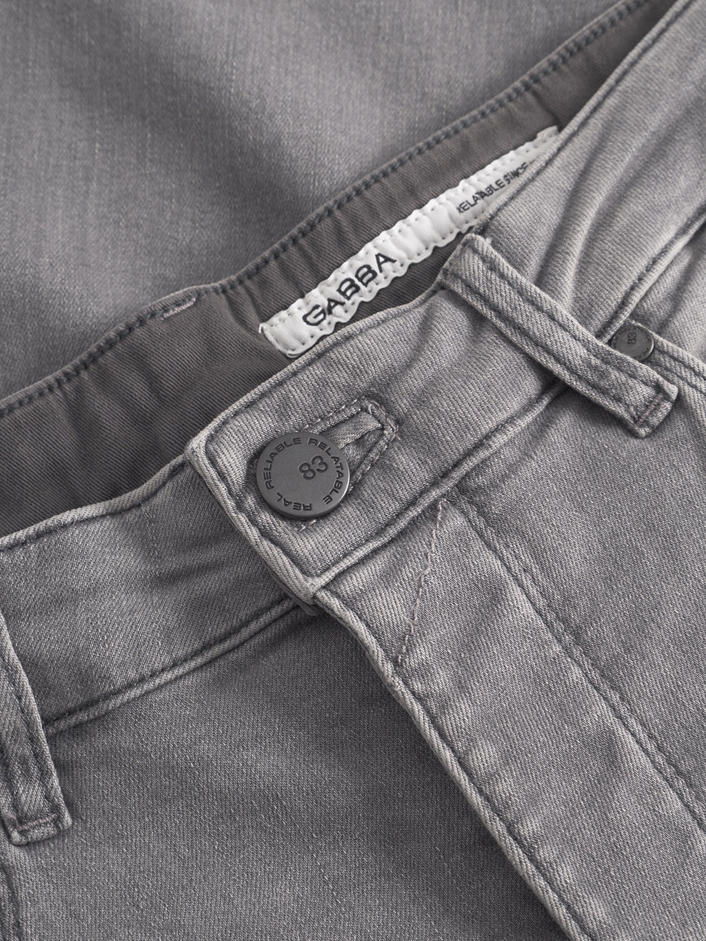 Close-up of GABBA GABrey K3454 - Denim wash slim fit gray jeans featuring a visible waistband, black metal button, belt loops, stitching details, and a white GABBA tag partially tucked inside.