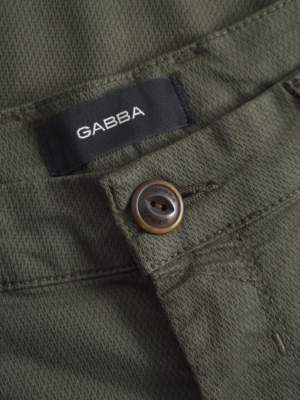 Close-up of GABBA’s GABpaul K3280 Dale Chino - Army: classic style olive green slim chinos, featuring a brown button engraved with GABBA and a black inner waistband label displaying the brand name.