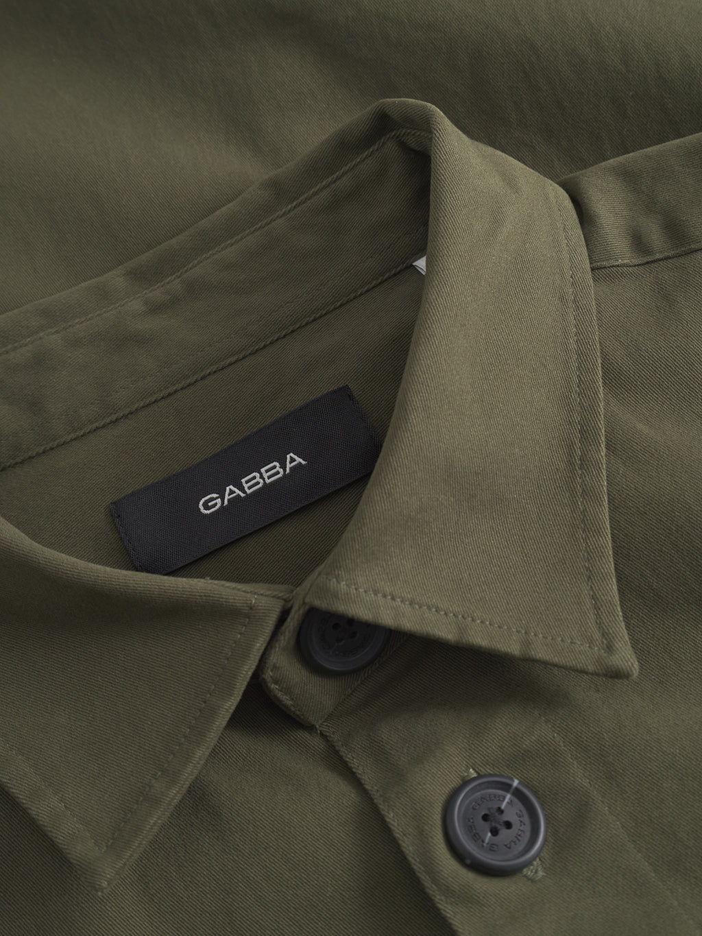 Close-up of the GABtopper LS Shirt - Army by GABBA, featuring black buttons, chest pockets, and a black GABBA label on the inside collar.