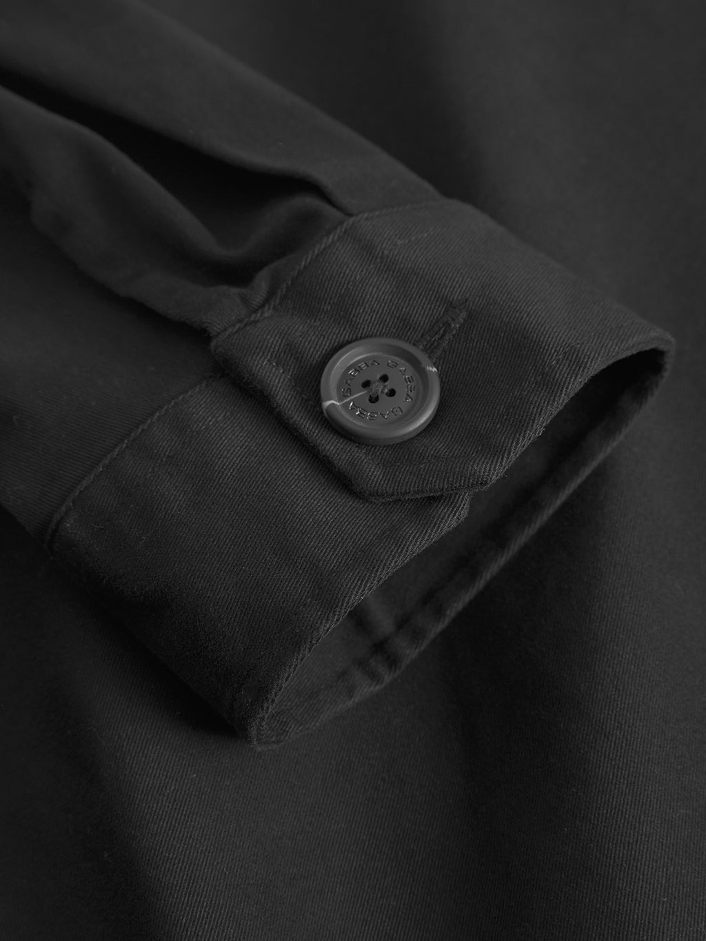 A close-up of the GABtopper LS Shirt - Black by GABBA shows its smooth, neatly stitched sleeve with a secure black buttoned cuff—ideal to pair with the shirt's collar or chest pockets for a refined look.
