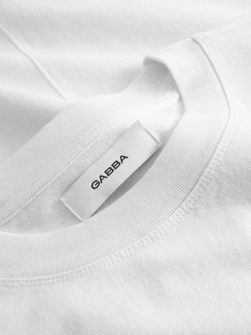 Close-up of the GABnigel Wix Boxy Hour SS t-shirt in white by Gabba, showing a visible neck tag with the brand name and smooth, heavyweight cotton fabric with neat stitching.