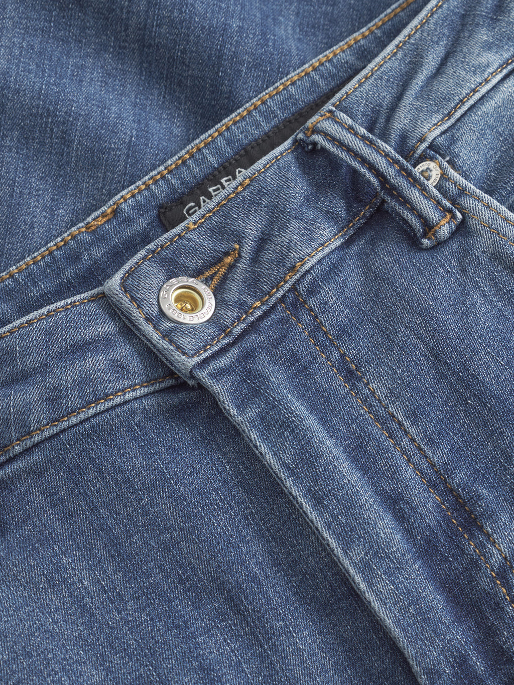Close-up of Gabba GABjones Vanew slim jeans in mid blue denim, featuring super-stretch fabric, waistband with metal button, belt loop, visible stitching, and partially visible brand label above the button.