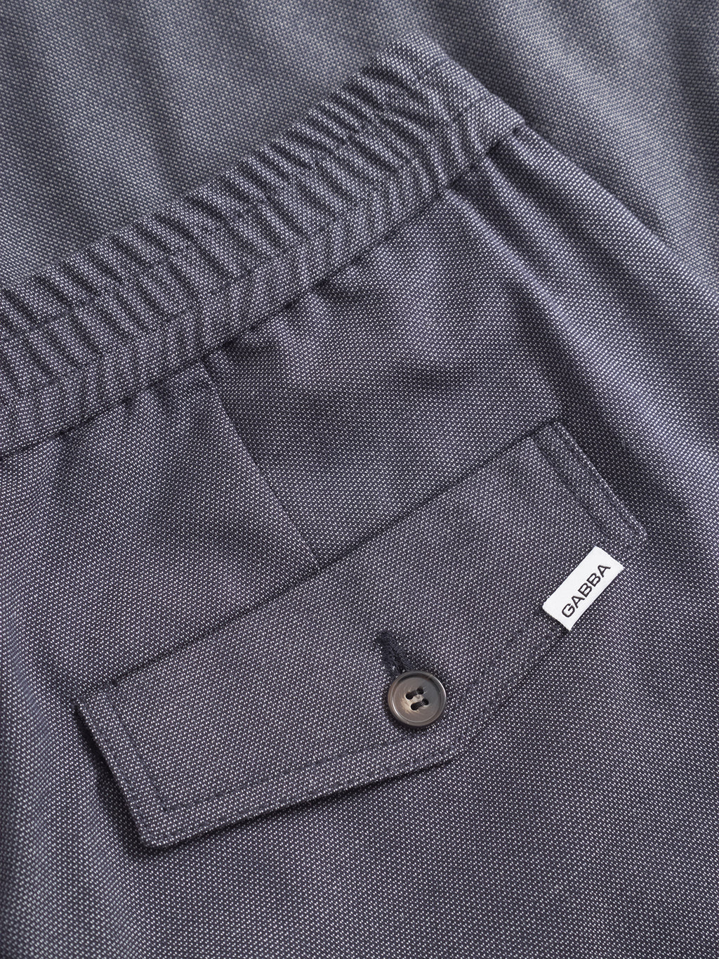 Close-up of the back pocket of Gabba’s Monza Button Carre - Navy pants, featuring a textured fabric, elastic waistband, buttoned flap pocket, and a small white “Gabba” label on the pocket for a versatile look.
