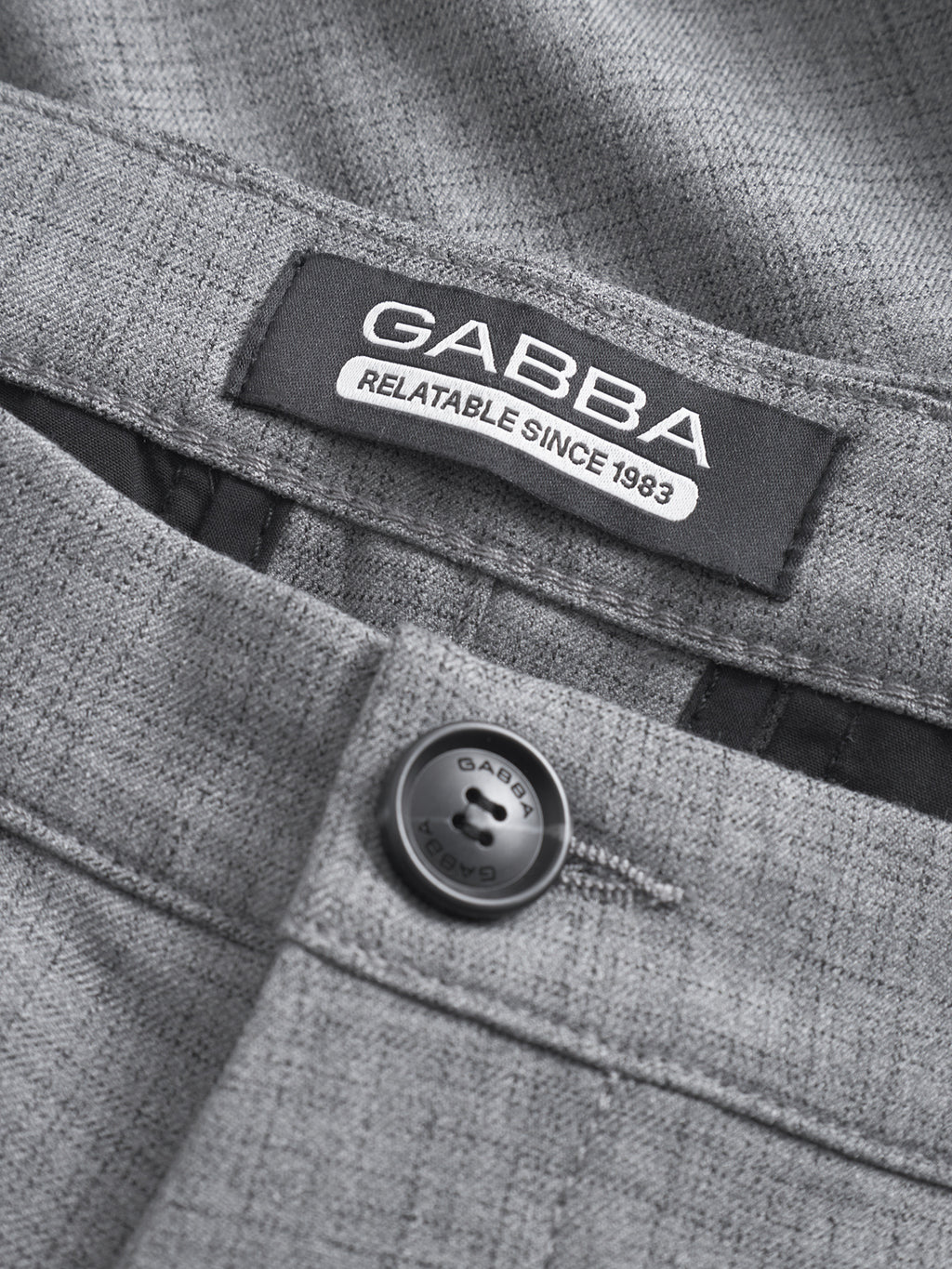 Close-up of GABBA Pisa Cross Lt Grey pants in light grey, made from a high-stretch cotton blend with a subtle pattern, featuring a black GABBA-engraved button and a GABBA RELATABLE SINCE 1983 label above the zipper.