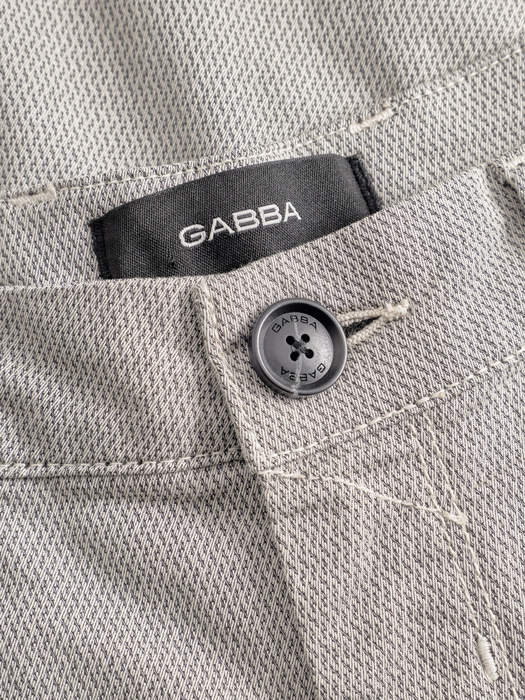 Close-up of the waistband of the GABpaul K3280 Dale Chino - Birch by Gabba, showing a black Gabba button and inner label, with classic French pockets and light gray textured slim fit fabric.