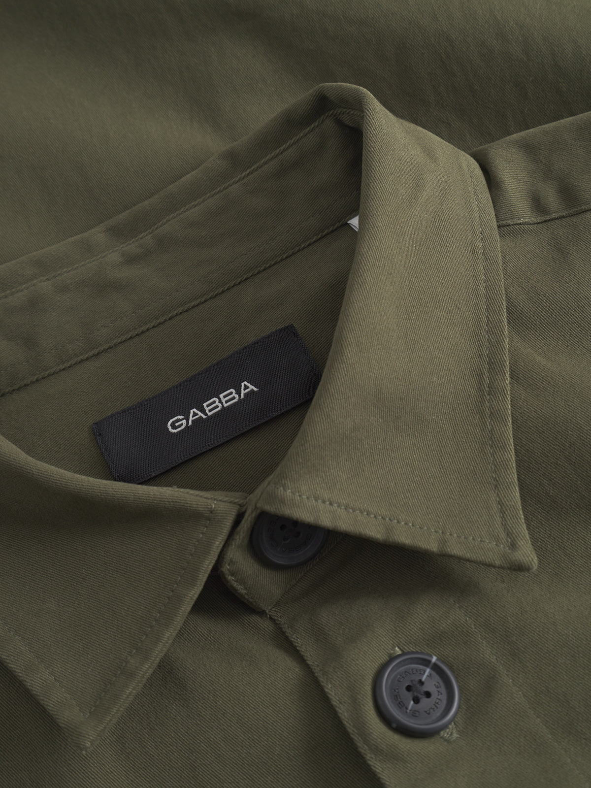Close-up of the GABBA GABtopper LS Shirt - Army, featuring a shirt collar, black buttons, and a black GABBA label sewn inside the collar.