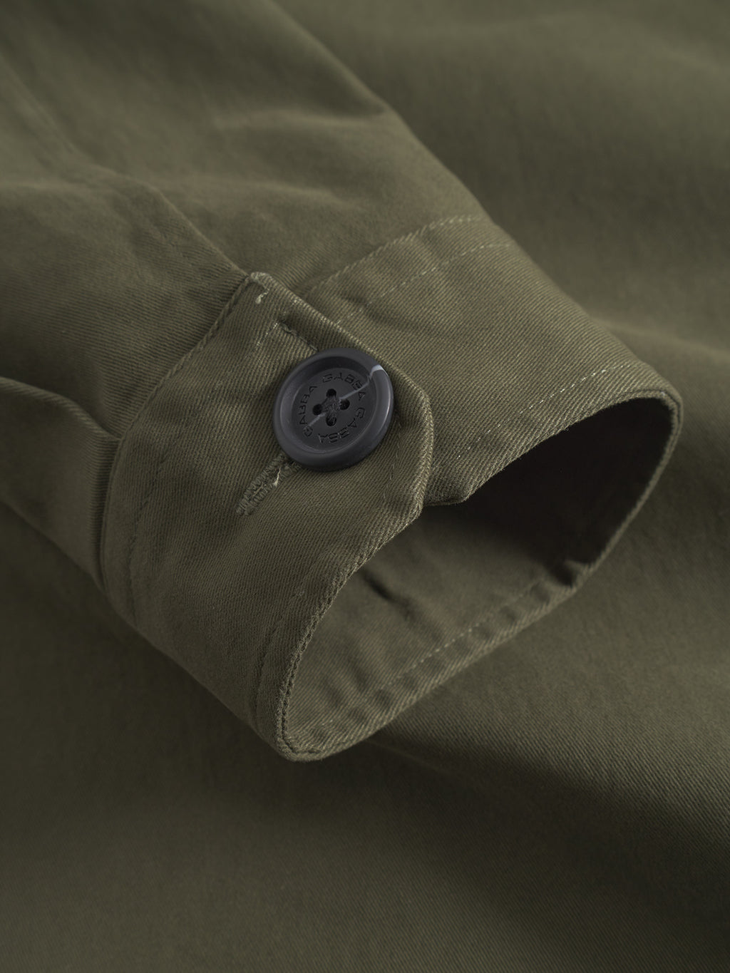 Close-up of the GABBA GABtopper LS Shirt - Army shows the olive green sleeve with a black button and detailed stitching, highlighting the fabric’s texture—ideal for pairing with its chest pockets and classic shirt collar.