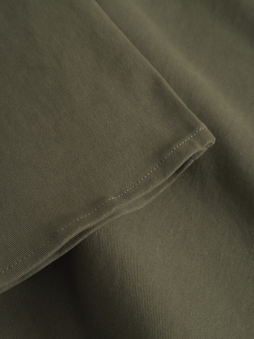 Close-up of the GABtopper LS Shirt - Army by GABBA, showing its olive-green fabric with visible edge stitching and a smooth, slightly textured surface.