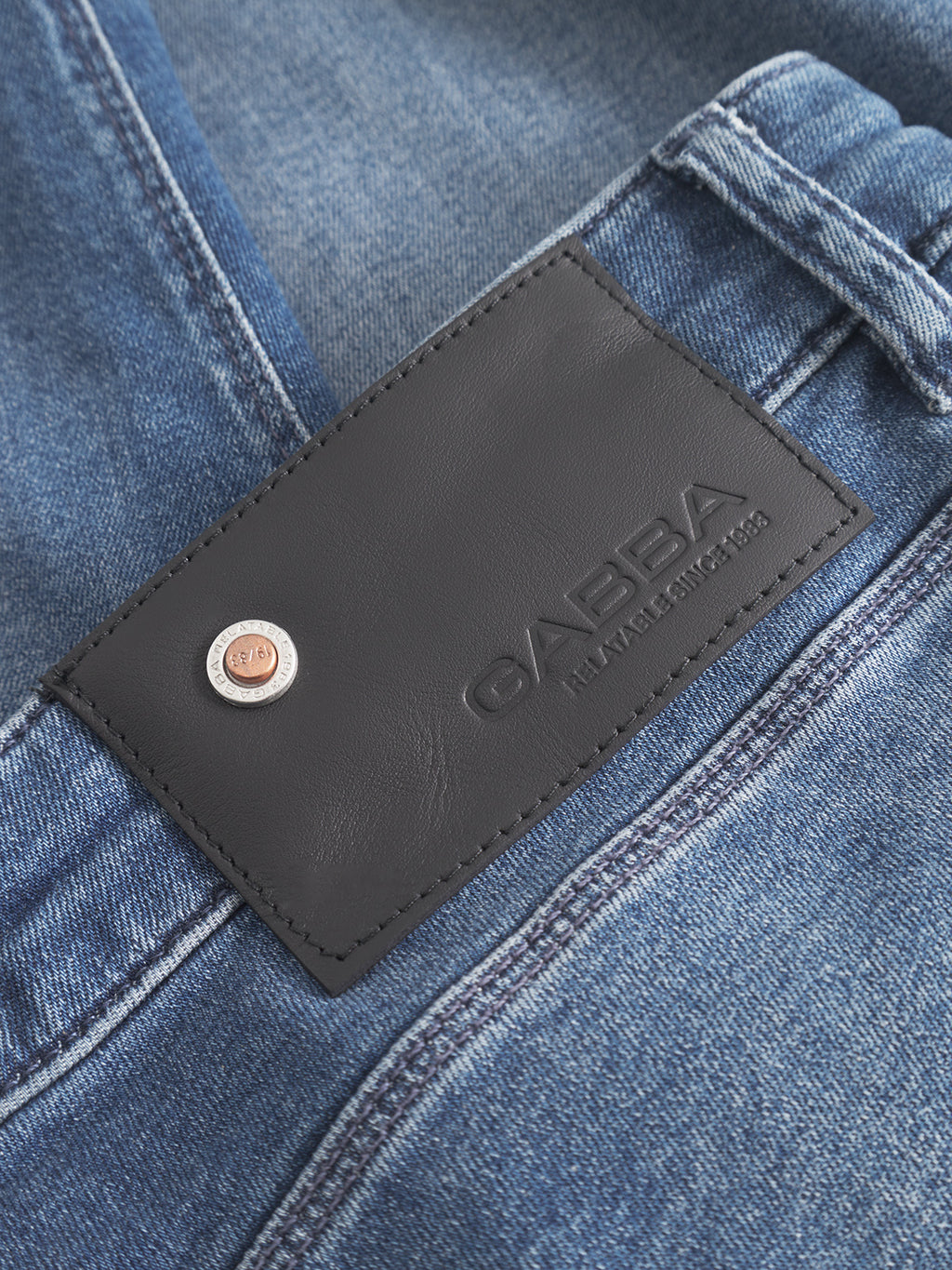 Close-up of GABBA GABrey K3866 TENCEL™ Jeans in denim wash, highlighting the black leather brand patch and metallic rivet on the waistband.