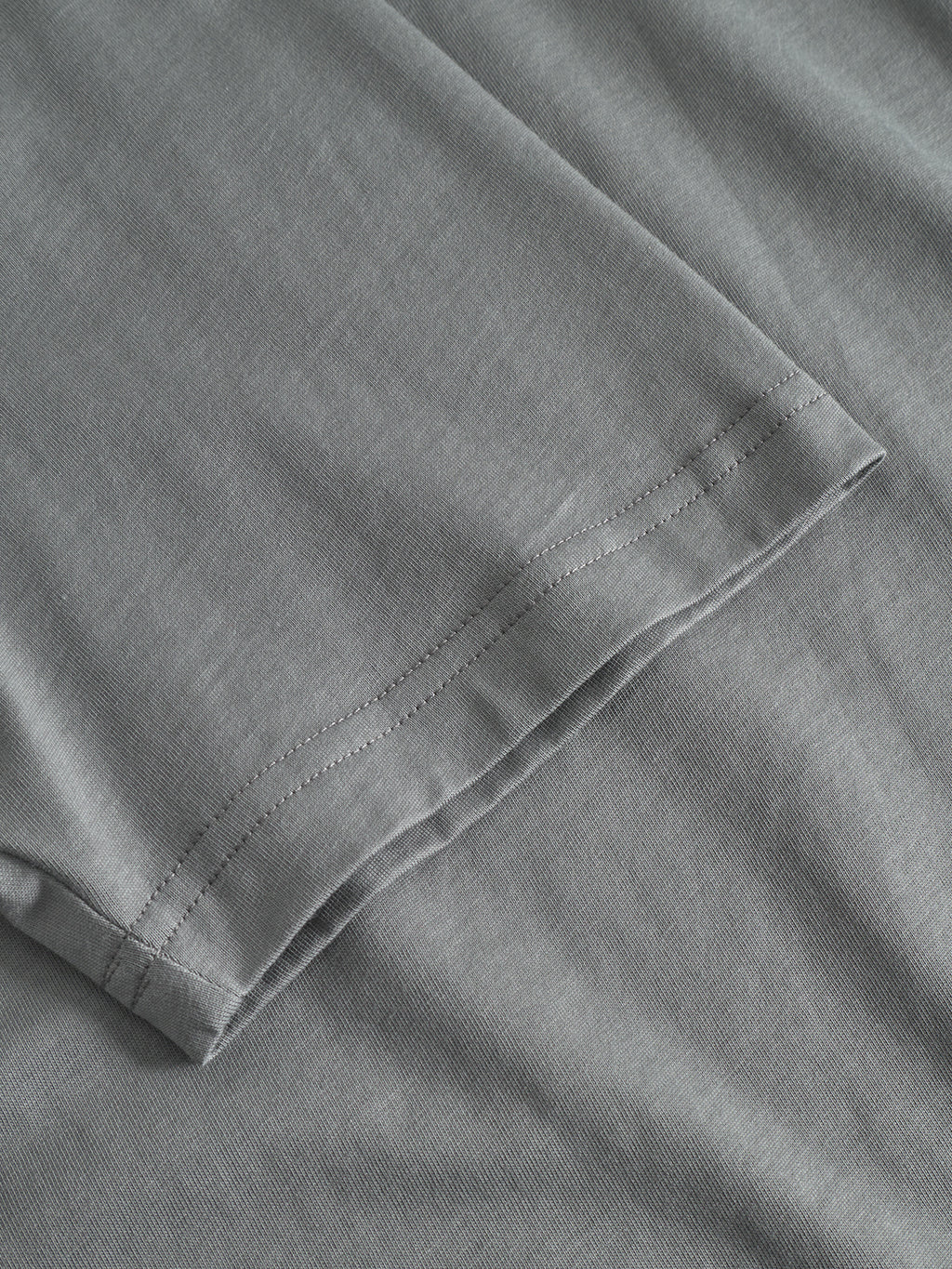 Close-up of the neatly stitched hem on the Gabba GABdune Logo GOTS SS T-Shirt in Dust Sage Green, showcasing its fine organic cotton texture and precise double-stitched seams.