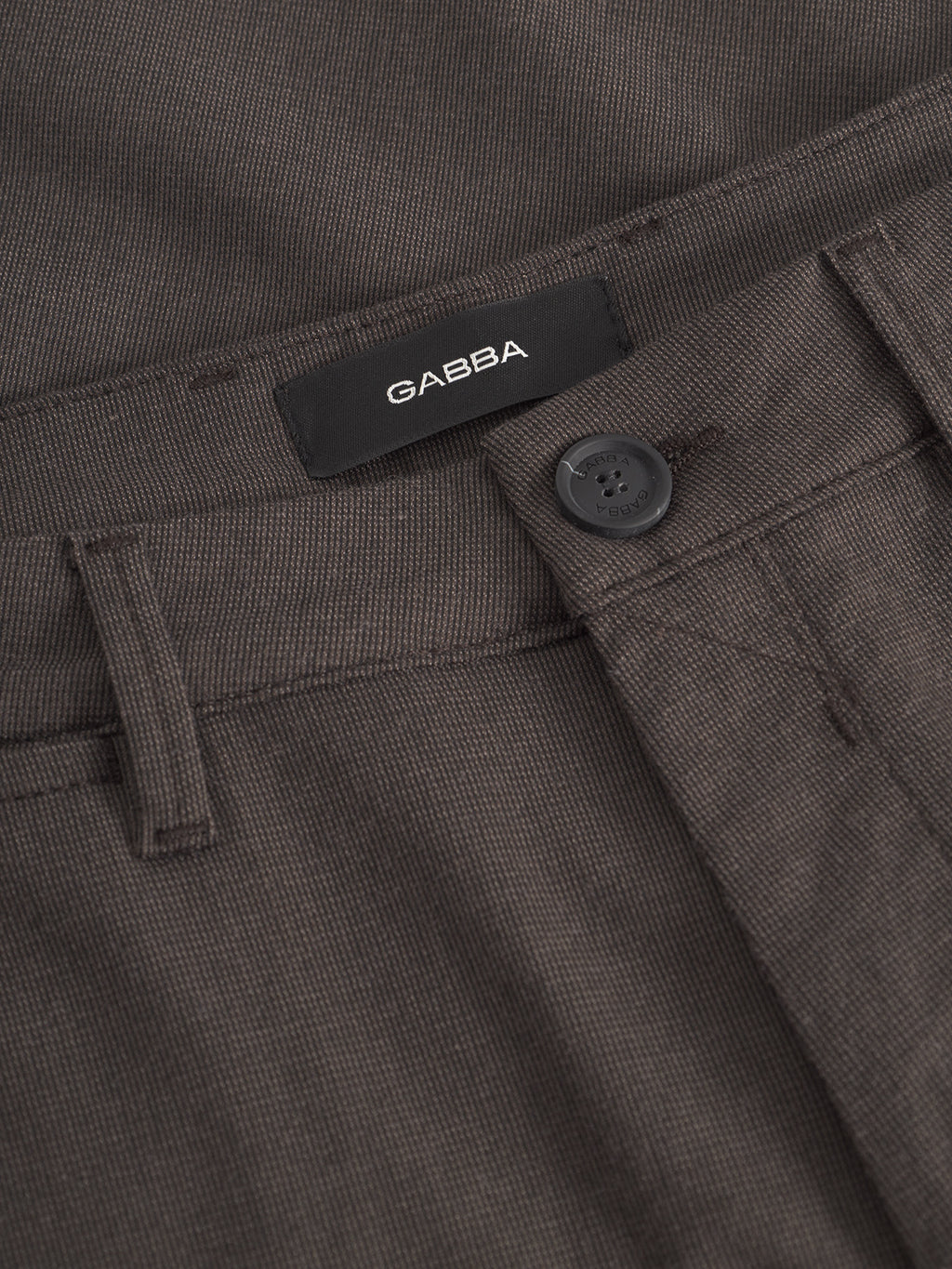 Close-up of the Gabba Paul Domo - Dk. Brown slim chino pant with a black Gabba label above the waistband, belt loop, button, partial zipper area, and stylish French pockets.