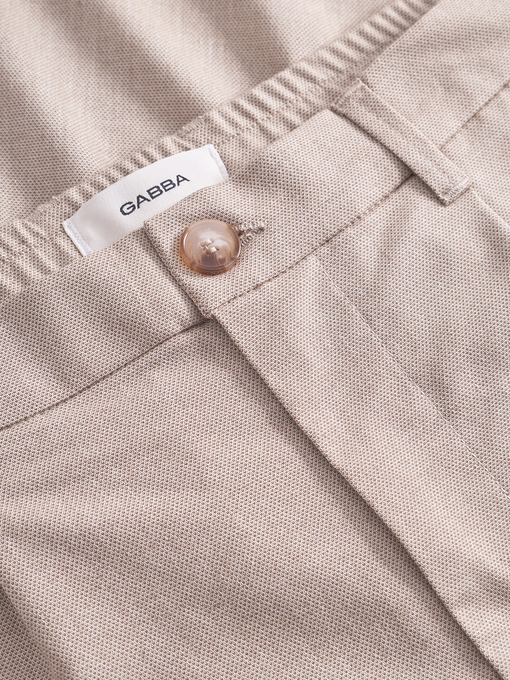 Close-up of Gabba's Napoli 19 Carre - Sand pants with textured fabric, brown button, and white label on the waistband. These versatile pants offer a perfect fit for any occasion.