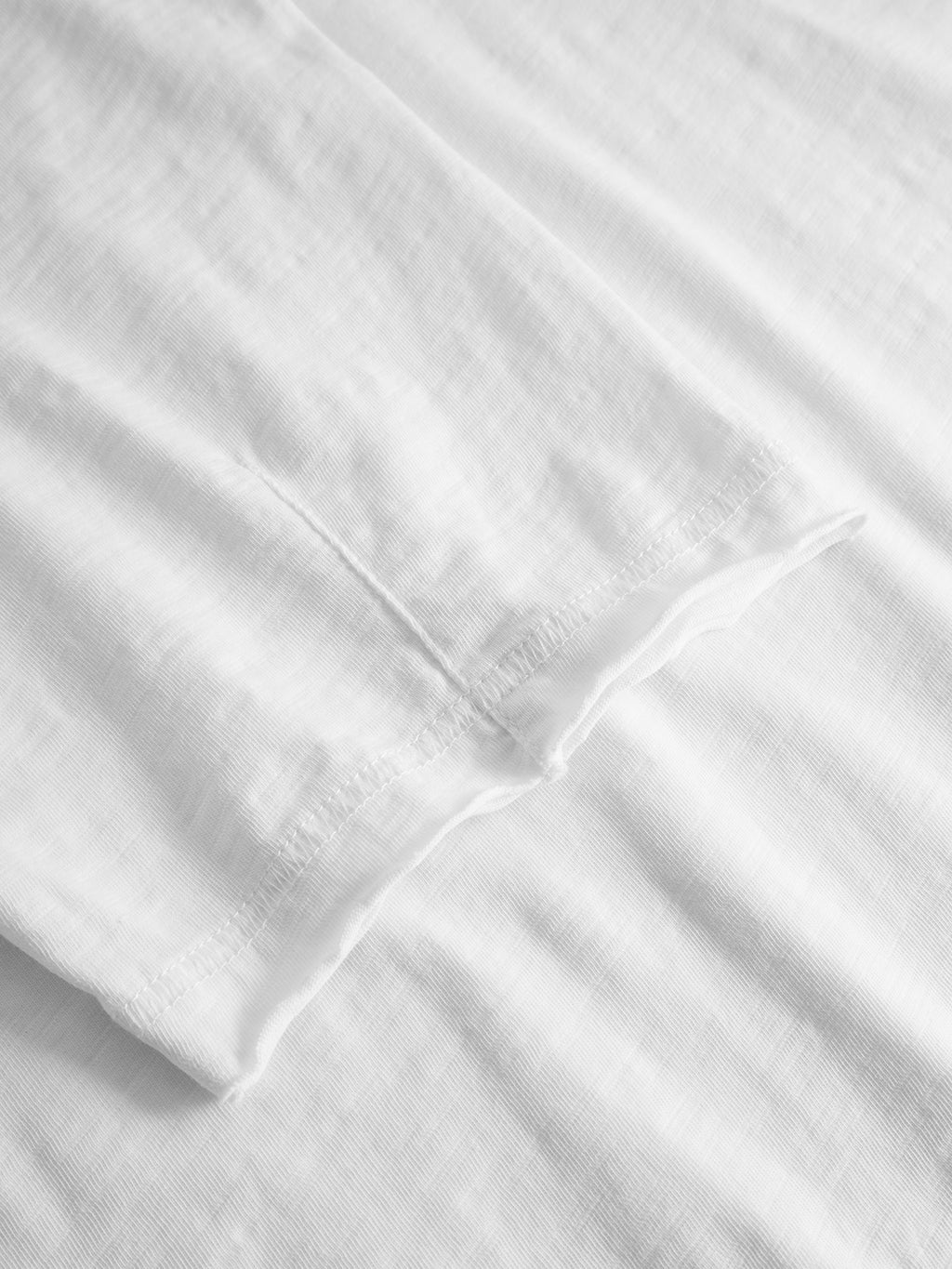 Close-up of the hems of two overlapping Gabba GABkostant New SS - White 100% cotton t-shirts, highlighting the textured fabric and stitching detail against a white background.