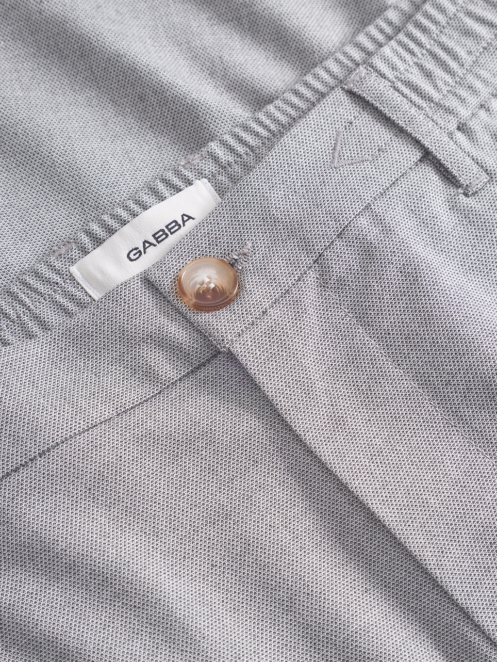 Close-up of Gabba Monza Button Carre pant in light grey—a relaxed straight fit with textured fabric, elastic waist, beige button, belt loop, and a visible white GABBA label.