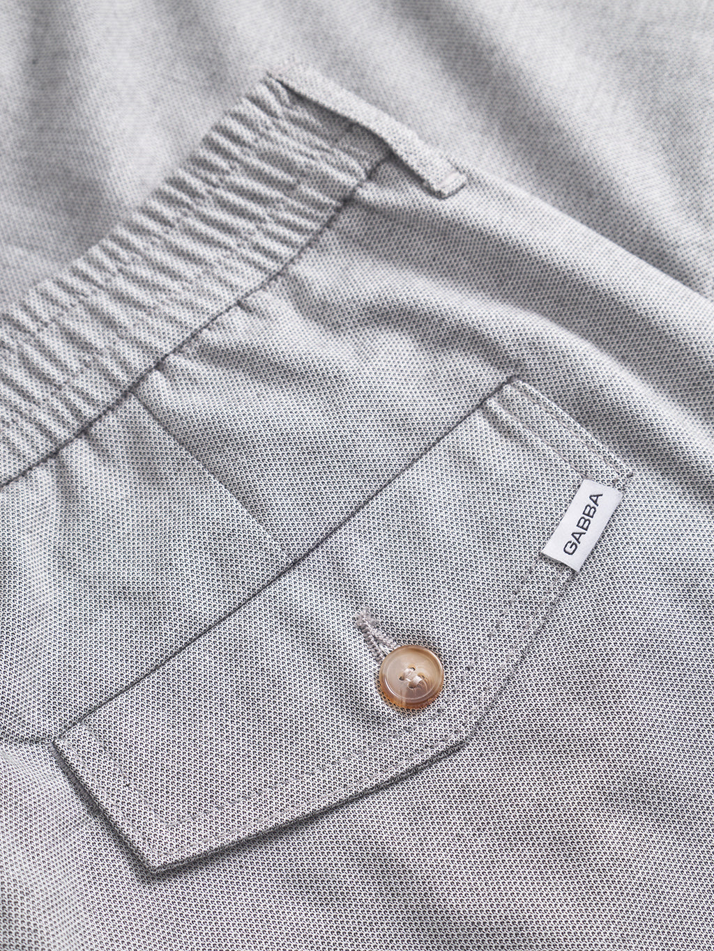 Close-up of the Monza Button Carre - Lt. Grey relaxed straight pant by Gabba, featuring an elastic waistband, buttoned flap pocket, and a small white Gabba tag accentuating its versatile style.