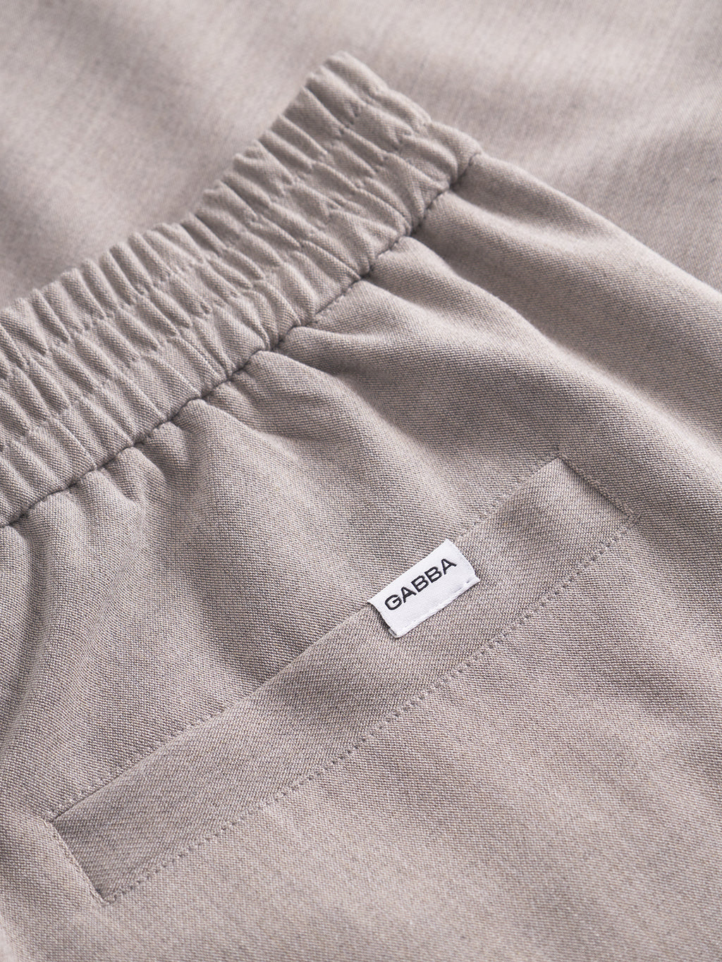 Close-up of the Gabba GABnapoli 19 Phin GRS pants in Sand, wool blend chinos featuring an elastic waistband, back pocket, and a white fabric label with “OAEBA” sewn above the pocket.