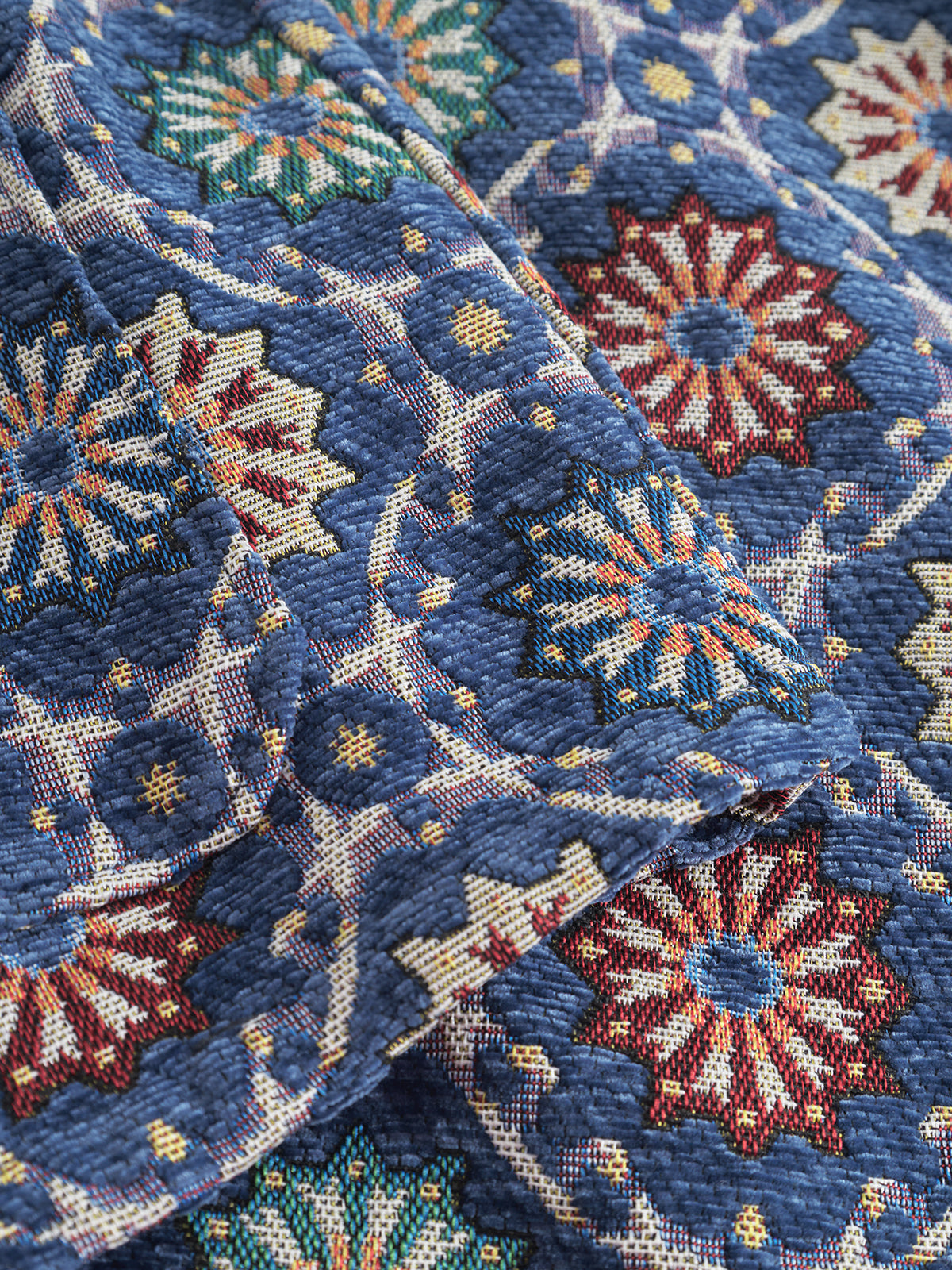 A close-up of the Gabba GABsimone Nava LS - Multi Pattern showcases its blue jacquard fabric, featuring intricate multicolored geometric floral designs and a woven texture that emphasizes its abstract motifs.
