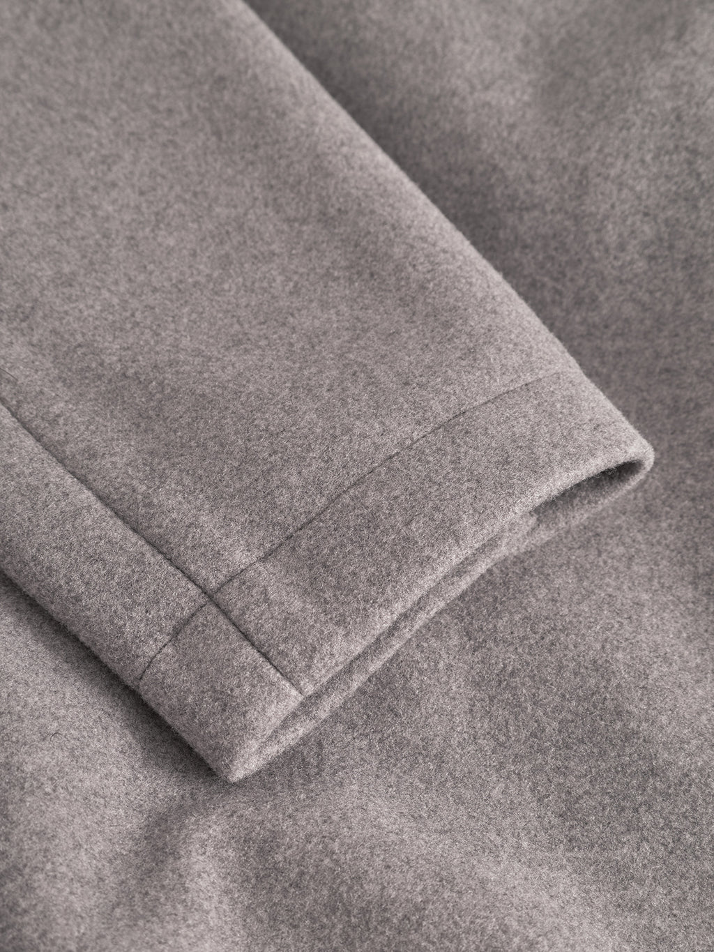 Close-up of Gabba's Orta Wox - Sand: a gray wool fabric with a neatly sewn seam and the edge of a bomber jacket sleeve, both lying flat on matching material.