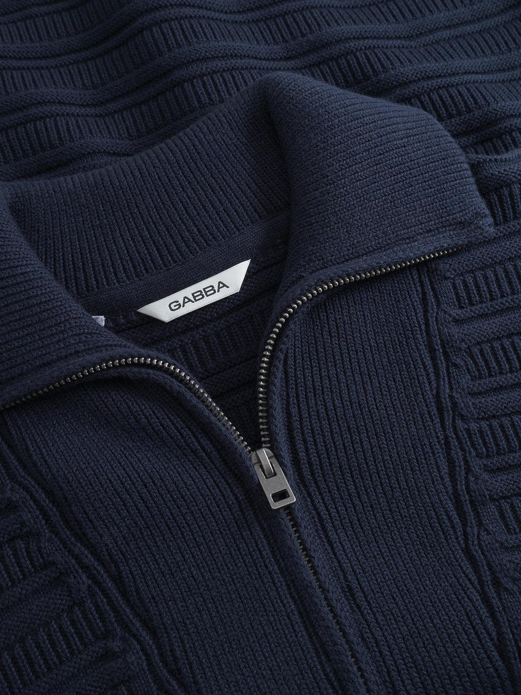 Close-up of the Gabba Iwaki Buco LS sweater in navy, featuring a knit texture, folded collar, silver half-zipper, and a white inner tag with the Gabba brand name.