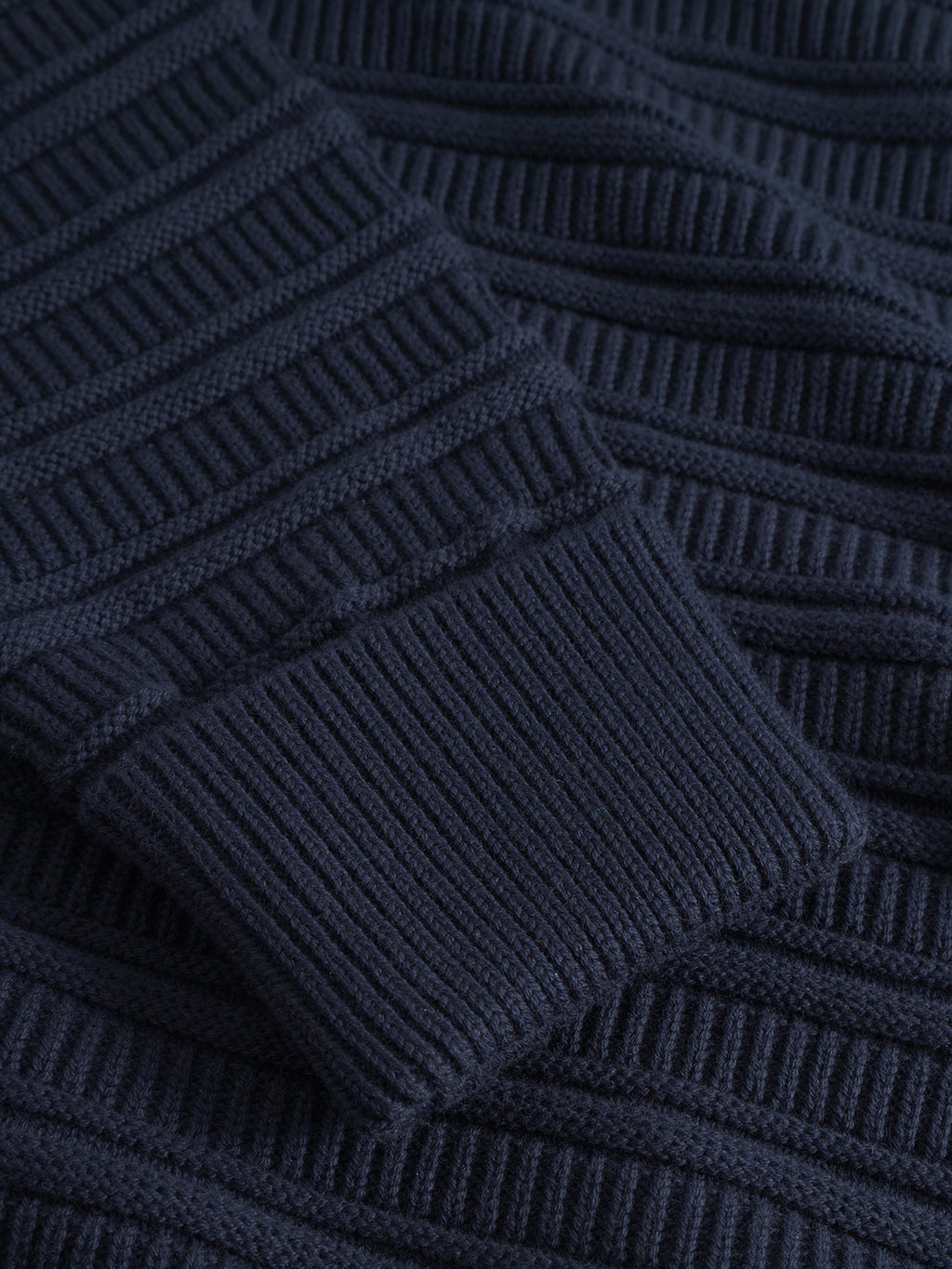 Close-up of the Gabba Iwaki Buco LS jumper in navy, highlighting its textured cotton knit, ribbed pattern, and the folded sleeve cuff.