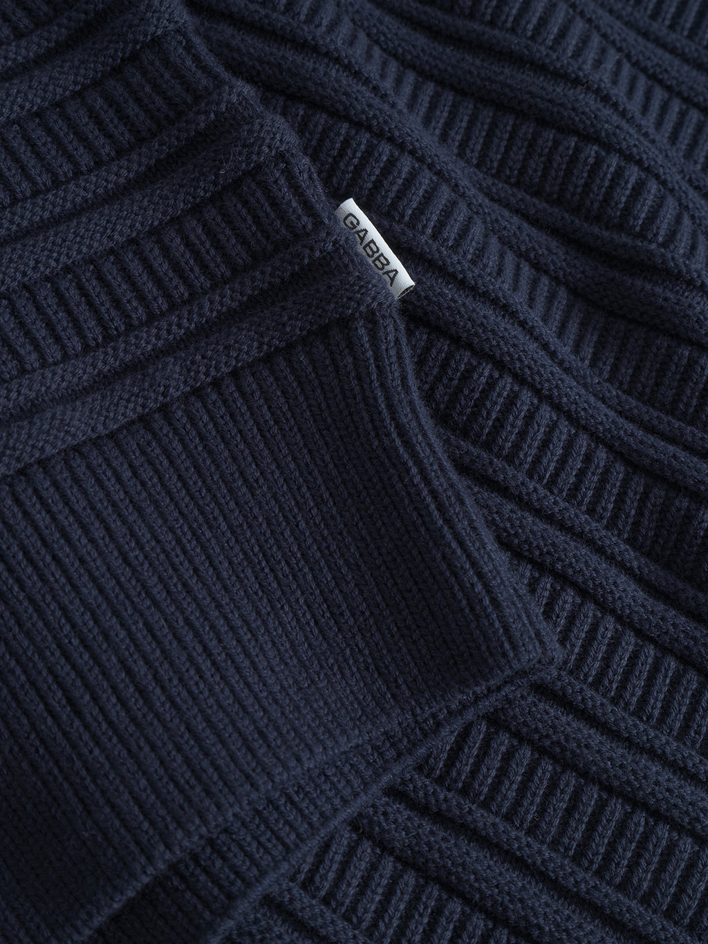 Close-up of the Gabba Iwaki Buco LS sweater in navy. The ribbed knit texture and white sewn-in Gabba tag are clearly visible on this cotton jumper.