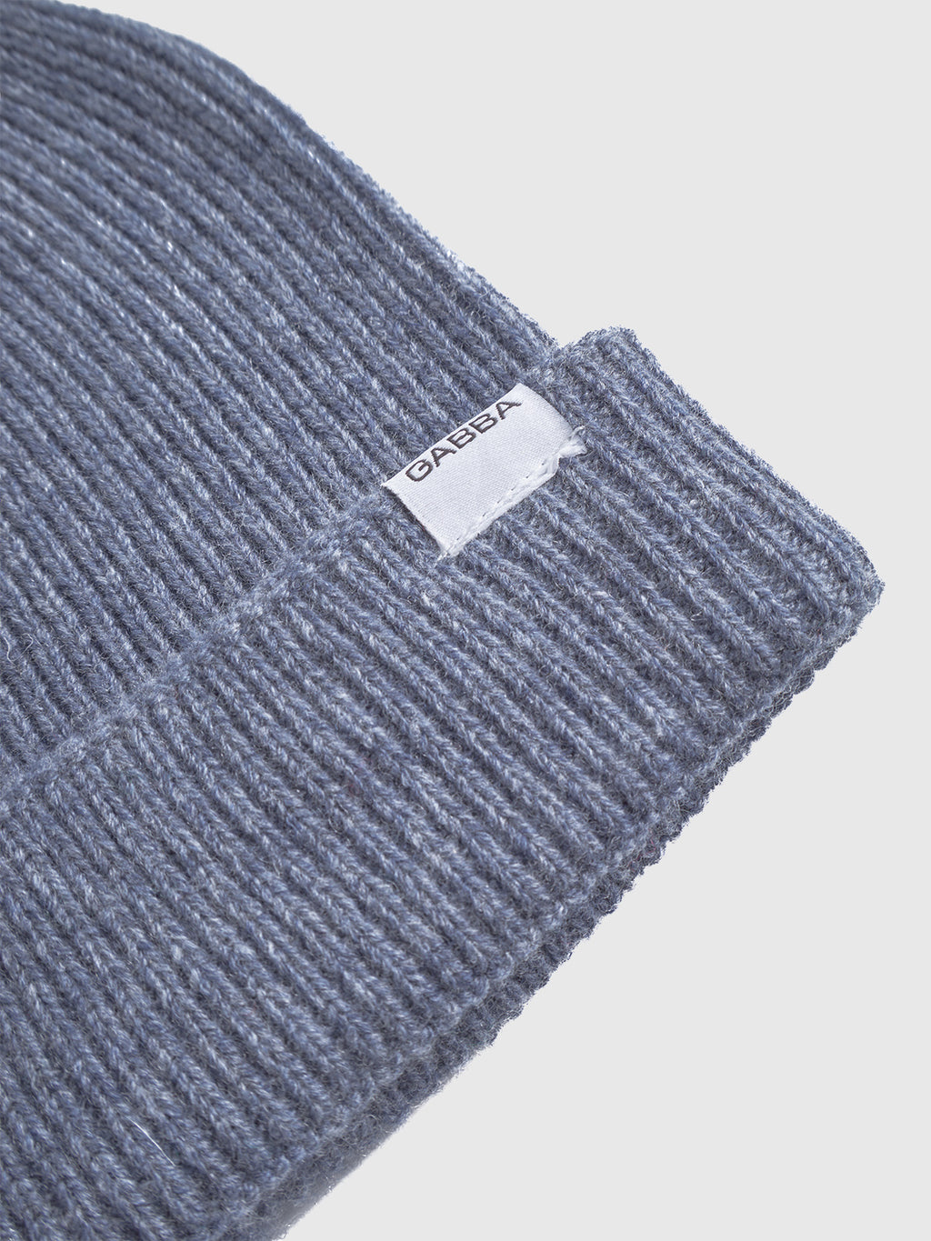 A close-up of the folded Biella Aico - Vintage Indigo ribbed knit beanie by Gabba in gray, featuring a white Gabba tag on the cuff for a cozy look with vintage indigo appeal.