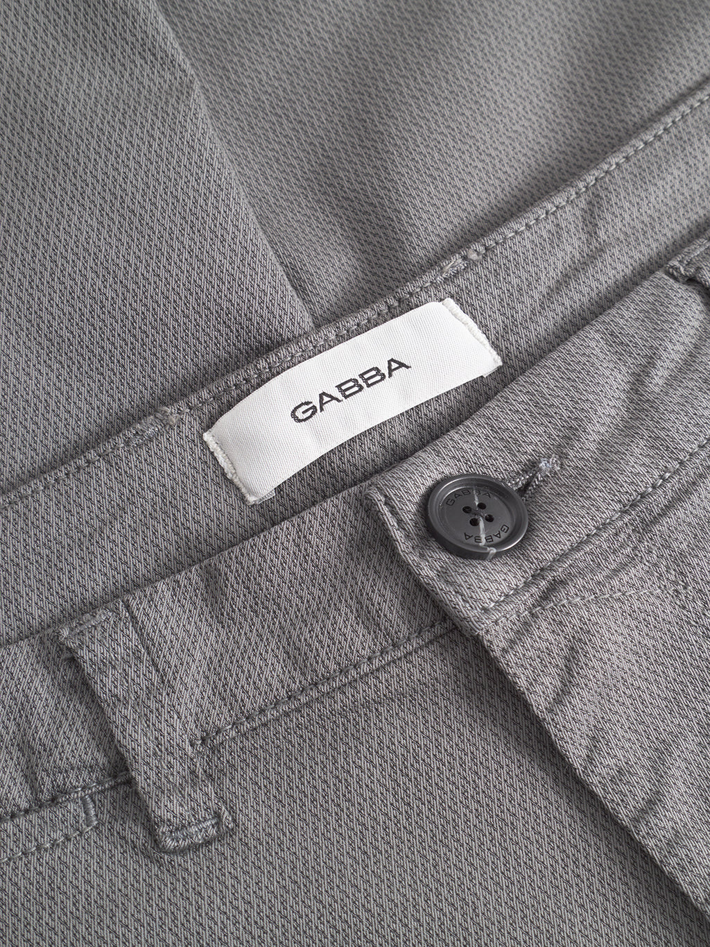 Close-up of the GABpaul K3280 Dale Chino in Dust Sage Green by Gabba, showing its textured slim fit, black button, French pockets, and a white Gabba label sewn inside the waistband.