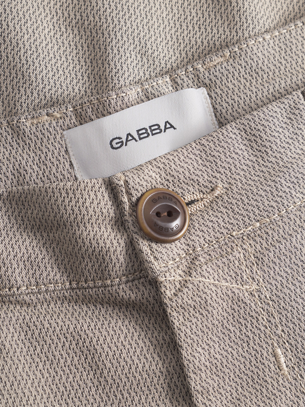 Close-up of GABBA GABpaul K3280 Dale Chino in Humus: beige textured slim-fit pants with French pockets, brown button, detailed stitching, and a white inner waistband label.