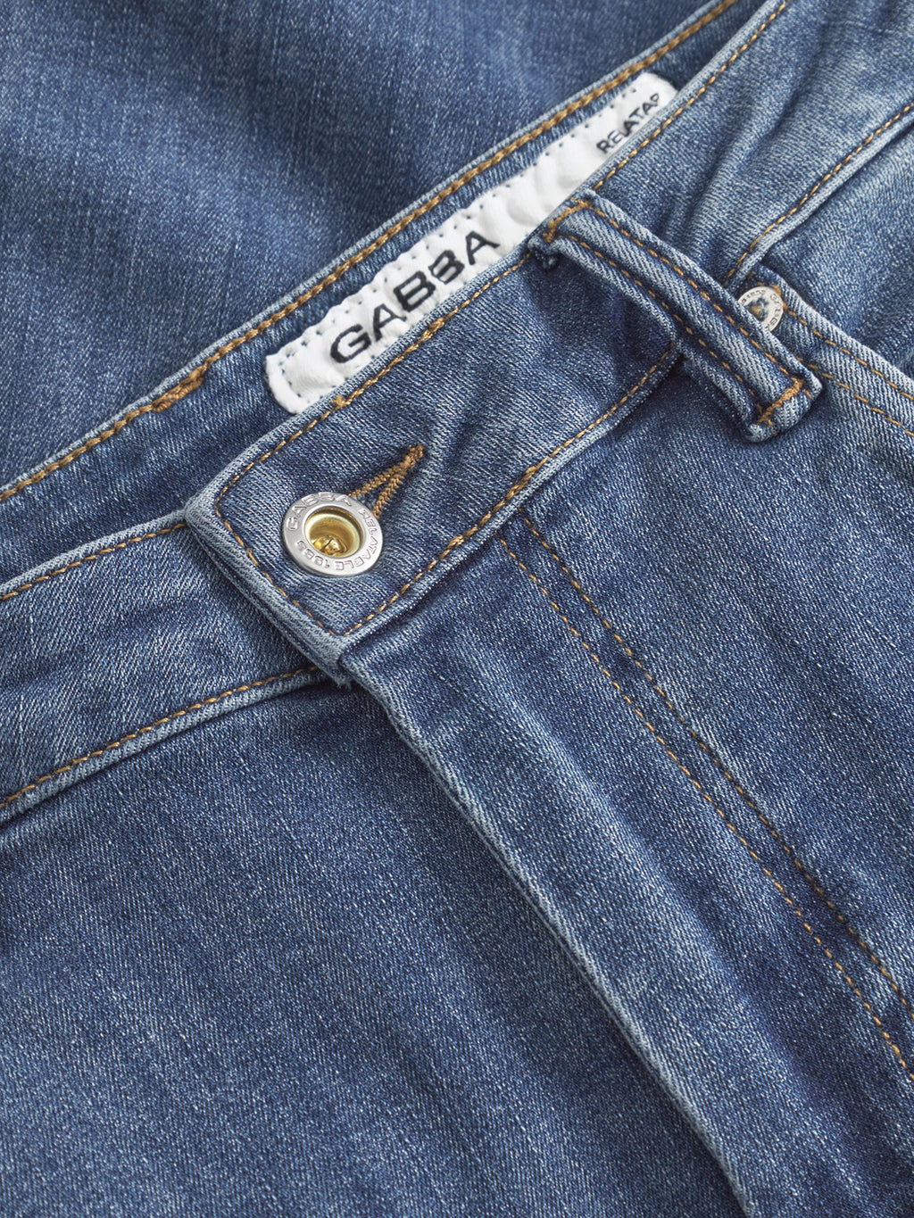 Close-up of Gabba GABjones Vanew mid blue denim slim jeans, showing a metal button, belt loop, and a white waistband label with the brand name Gabba.
