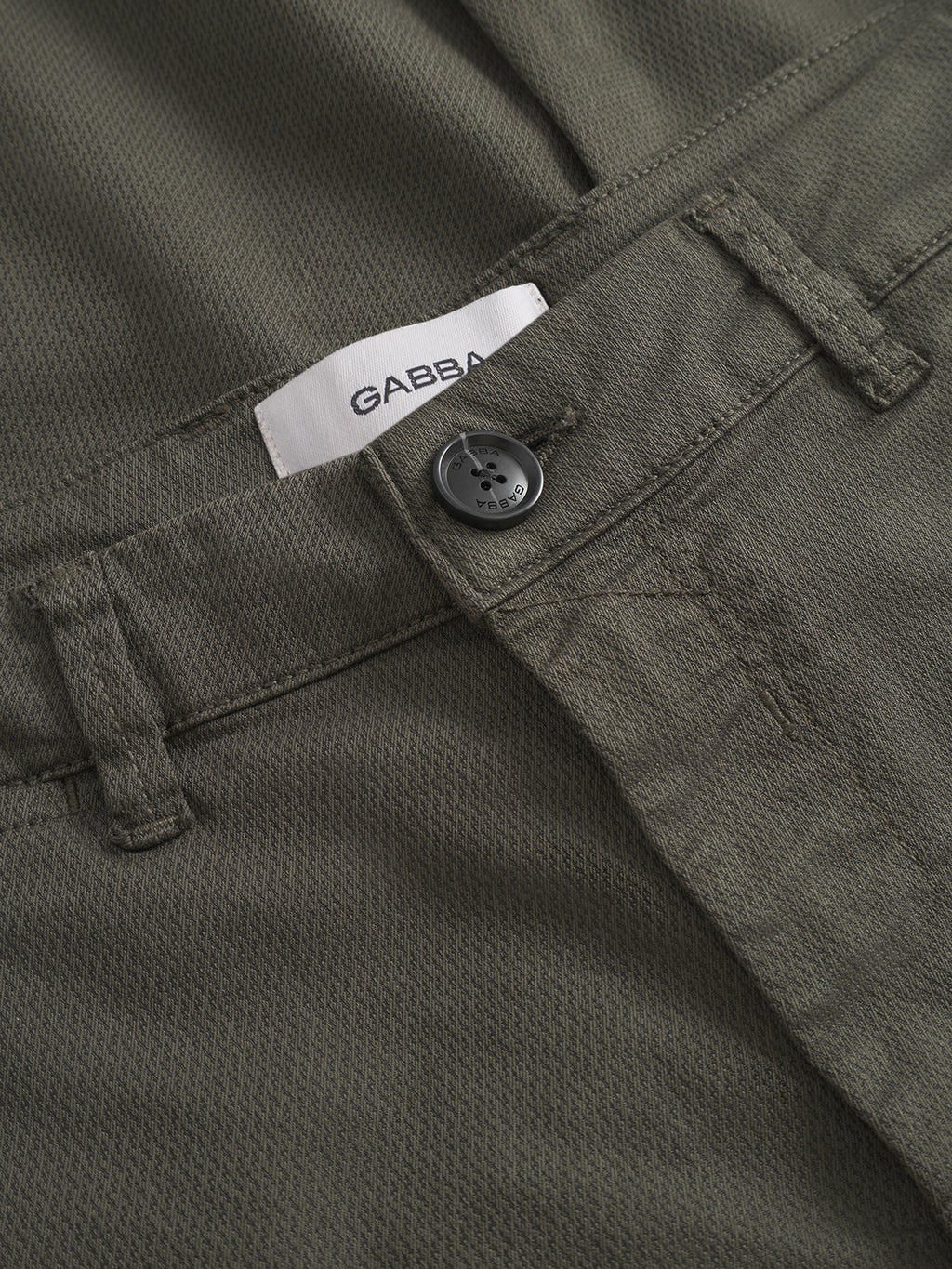 Close-up of Gabba’s Paul K3280 Cargo Dale - Army: olive green textured slim fit cargo pants with a black button, belt loops, and a white Gabba tag on the waistband—an elevated men’s fashion piece.