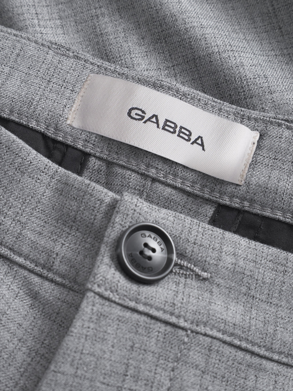 Close-up of GABBA Pisa Cross Lt Grey pants in a high-stretch cotton blend, featuring a white GABBA label above a black button engraved with GABBA and 1973 for a sharp metro style.