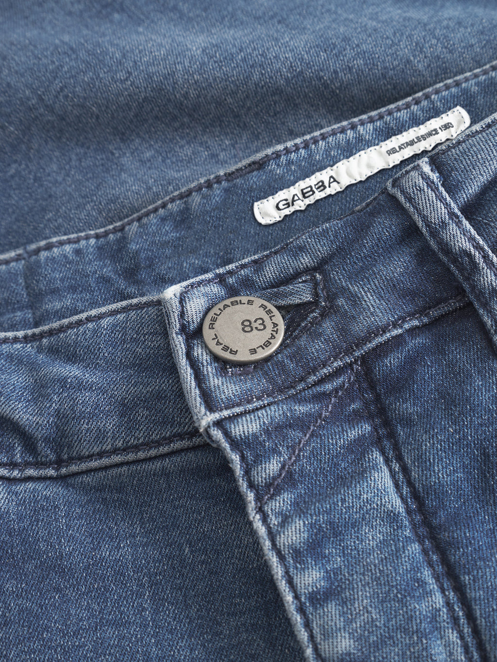 Close-up of GABBA GABrey K3866 TENCEL™ Jeans in denim wash, featuring the waistband, metal RELIABLE 1983 JEANS WEAR button, and a white GABBA fabric label stitched in black.
