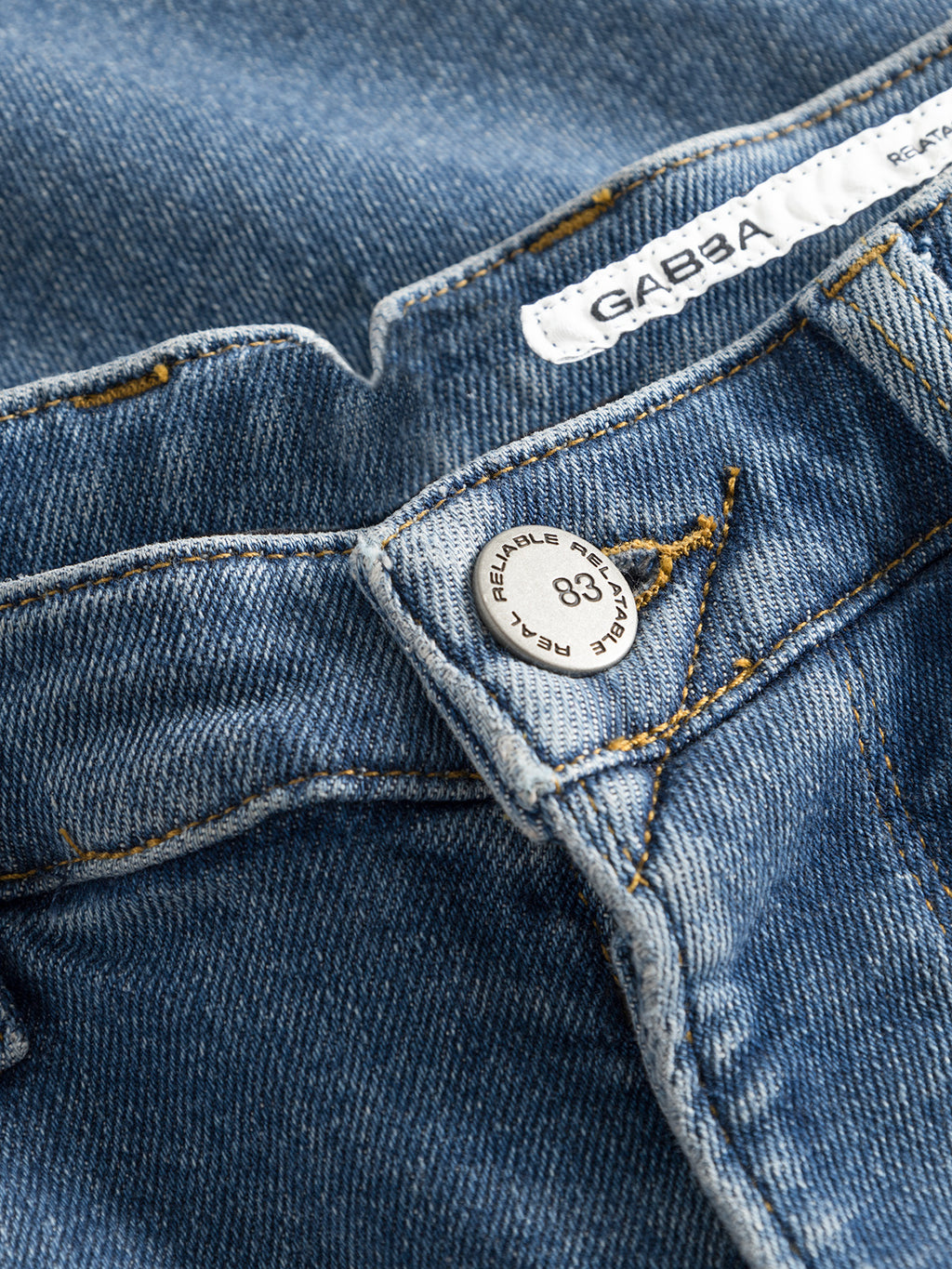 Close-up of GABBA Alex K3948 Jeans - Denim wash, showing a silver REAL REPAIR 83 button and white GABBA label on the worker waistbands. Yellow stitching details accentuate the blue denim for a stylish, modern look.