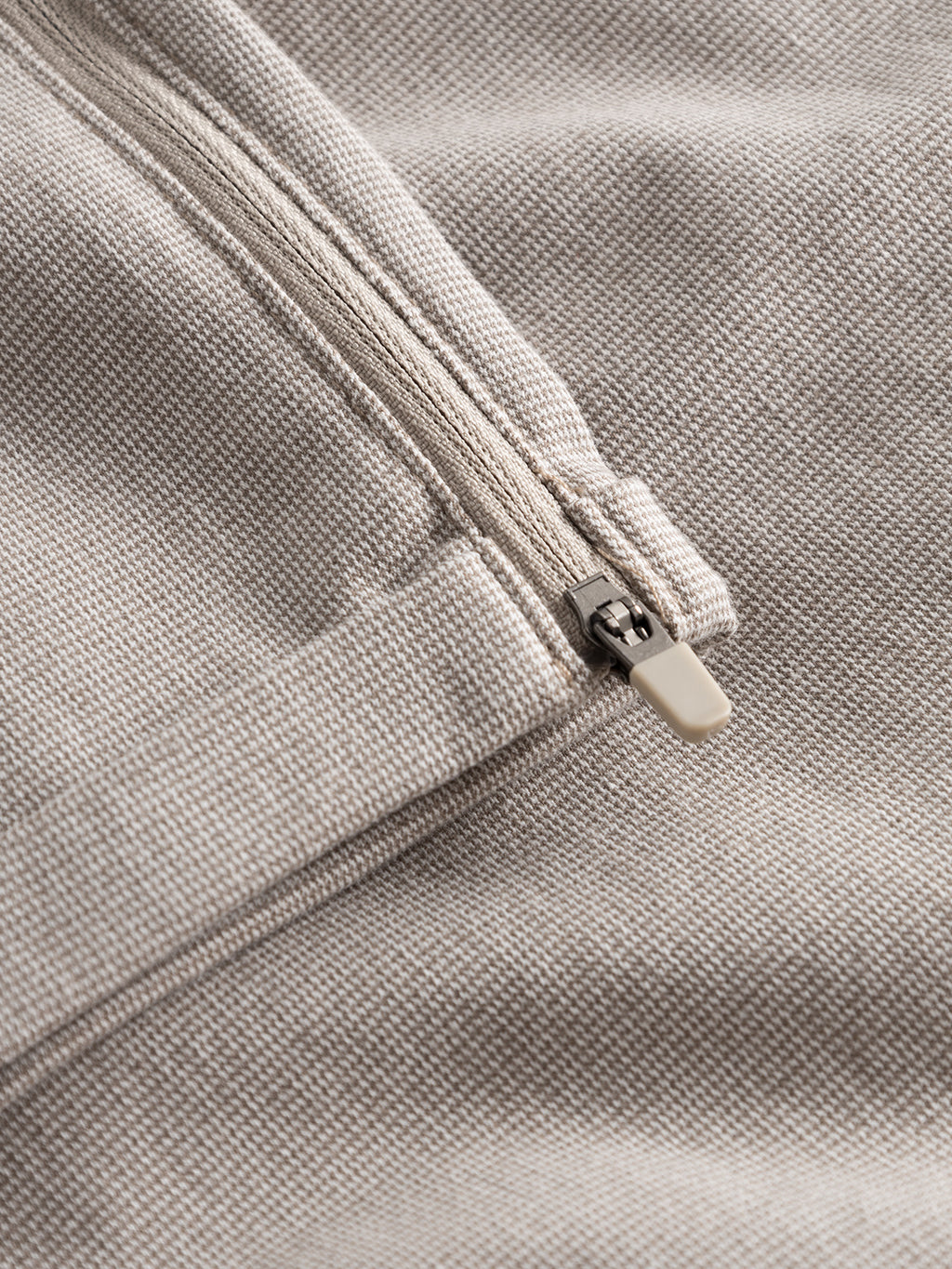 Close-up of Pisa Domo Pants - Coriander by Gabba, featuring a beige fabric and partially open metal zipper, highlighting the detailed texture and pull tab—ideal for showcasing material quality.