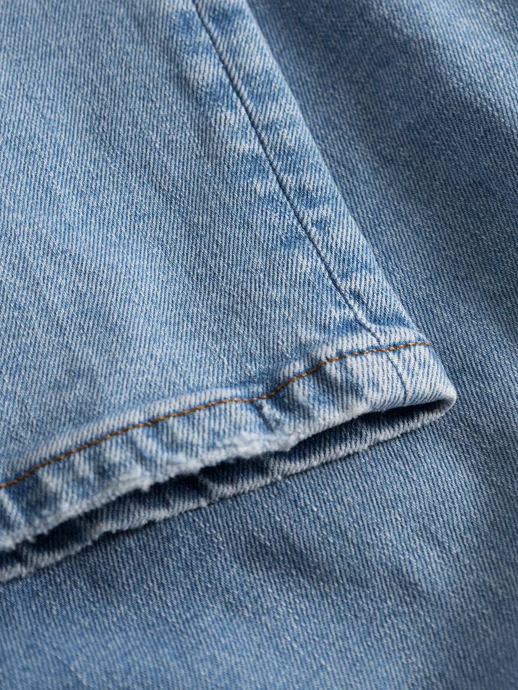 Close-up of Gabba GABmarc F1012 - Lt. Blue Denim fabric, showing visible stitching, a folded hem, and the textured weave typical of this light blue denim material.